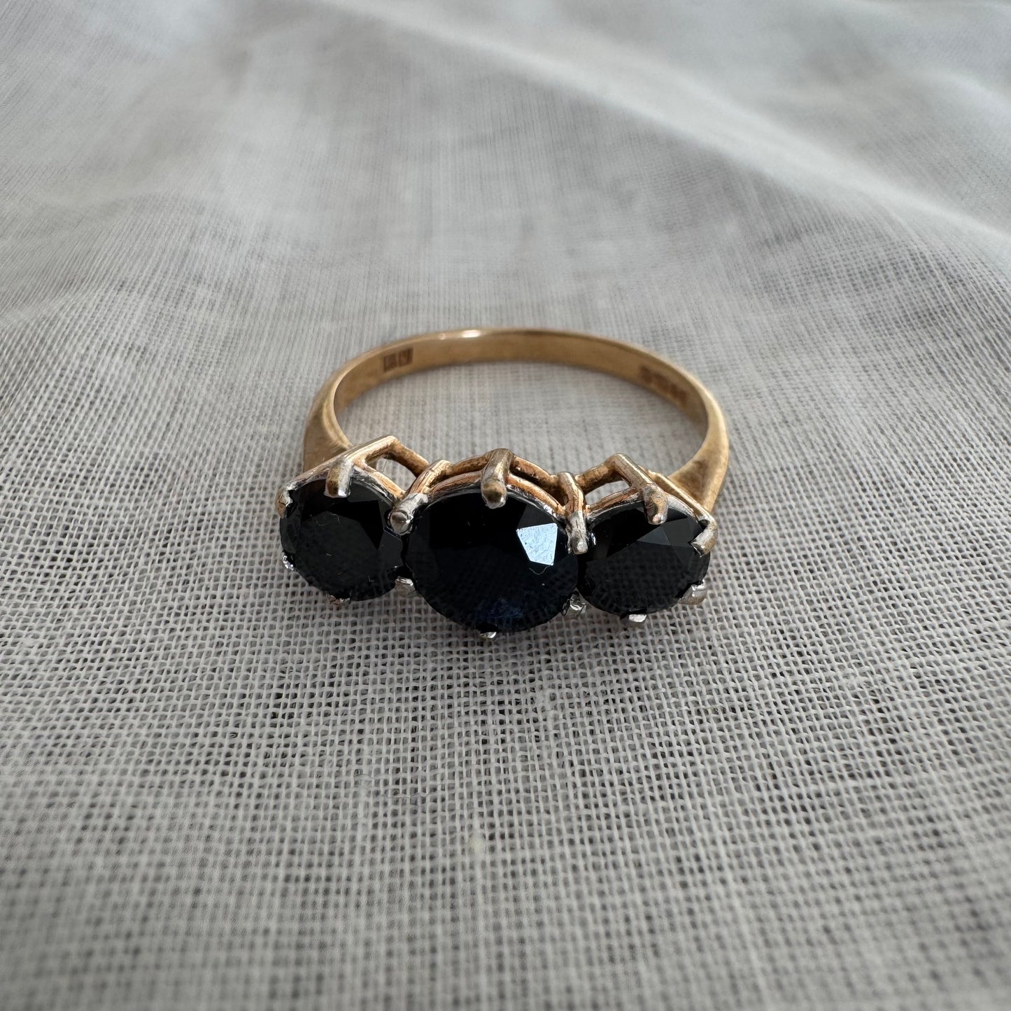 טבעת זהב 10 קראט משובצת שלוש אבני ספיר בצבע כחול כהה בחיתוך עגול, בעיצוב קלאסי עם נוכחות עמוקה ואלגנטית.