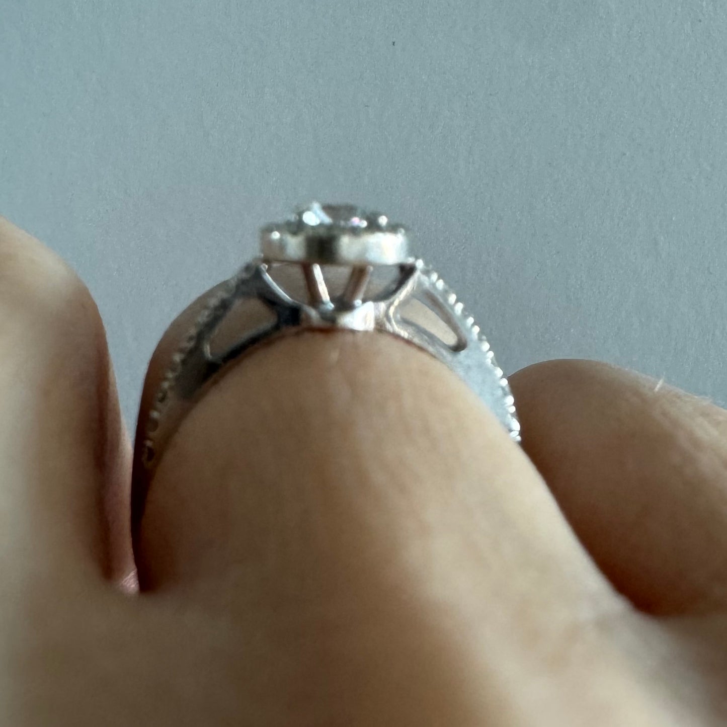 טבעת זהב לבן 14 קראט משובצת יהלום מרכזי עגול והילה נוצצת של יהלומים קטנים, עם יהלומים נוספים על החישוק.