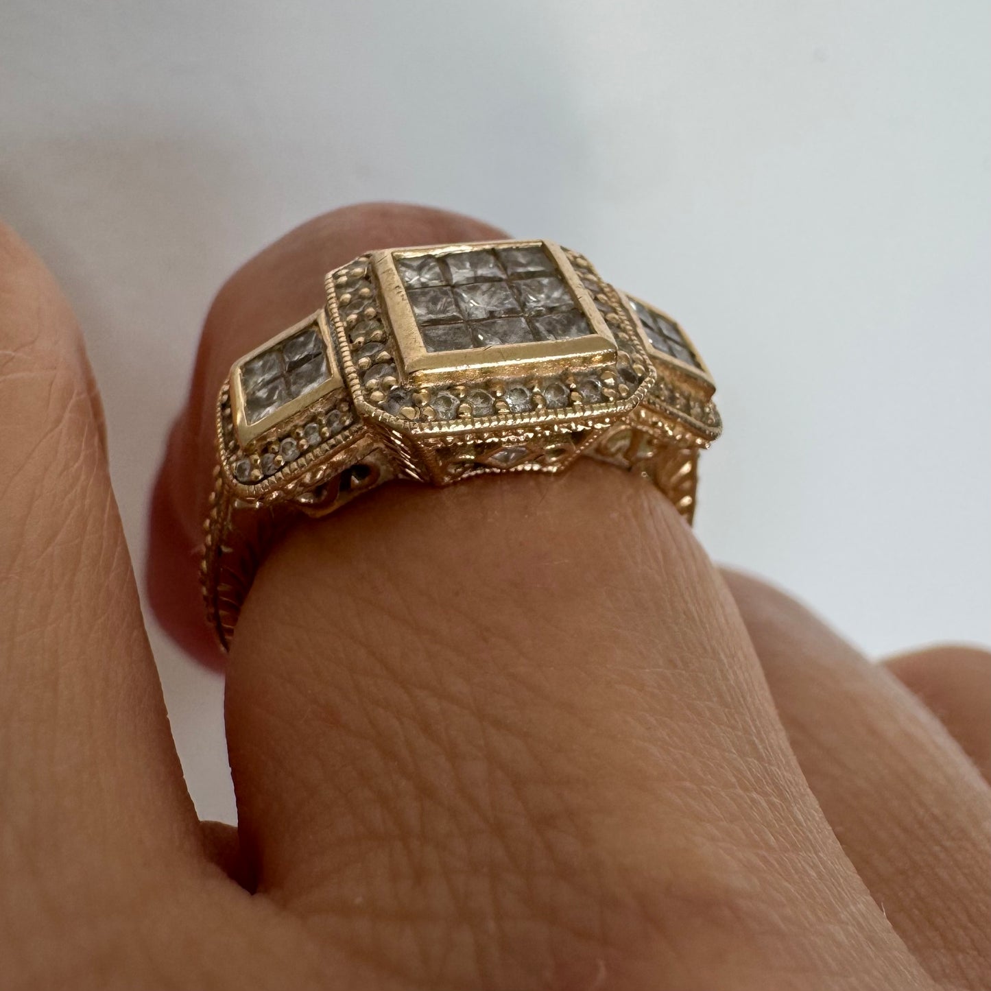 טבעת זהב צהוב 14 קראט משובצת יהלומים בחיתוך פרינסס במרכז, מוקפת הילה של יהלומים צדדיים.