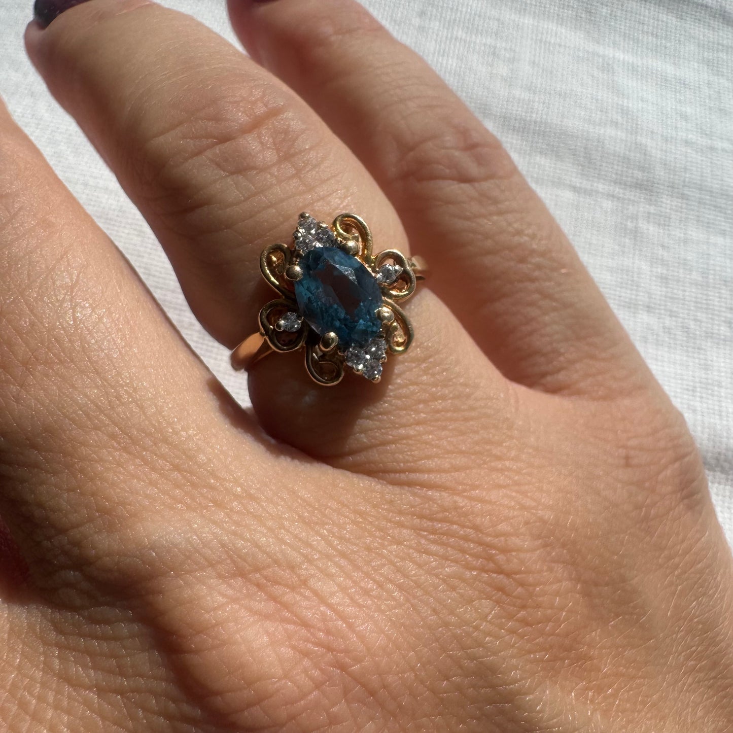 18K gold ring featuring an oval-cut Blue Topaz at the center, accented by sparkling side Diamonds and elegant scroll details.
