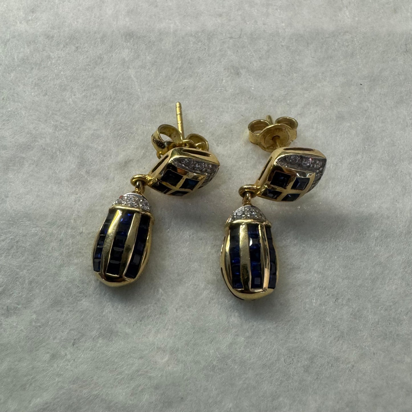עגילי זהב צהוב 18 קראט תלויים, משובצים אבני ספיר כחולות בגוון כחול עמוק בעיצוב גיאומטרי, בשילוב יהלומים מנצנצים