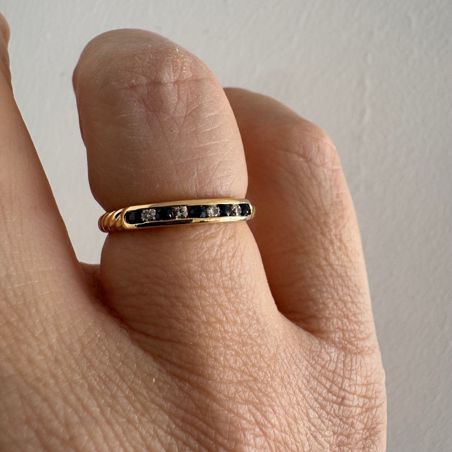 טבעת זהב צהוב 18 קראט בעיצוב נקי ומדויק, משובצת בשורה עדינה של אבני ספיר כחולות וביניהן יהלומים לבנים.