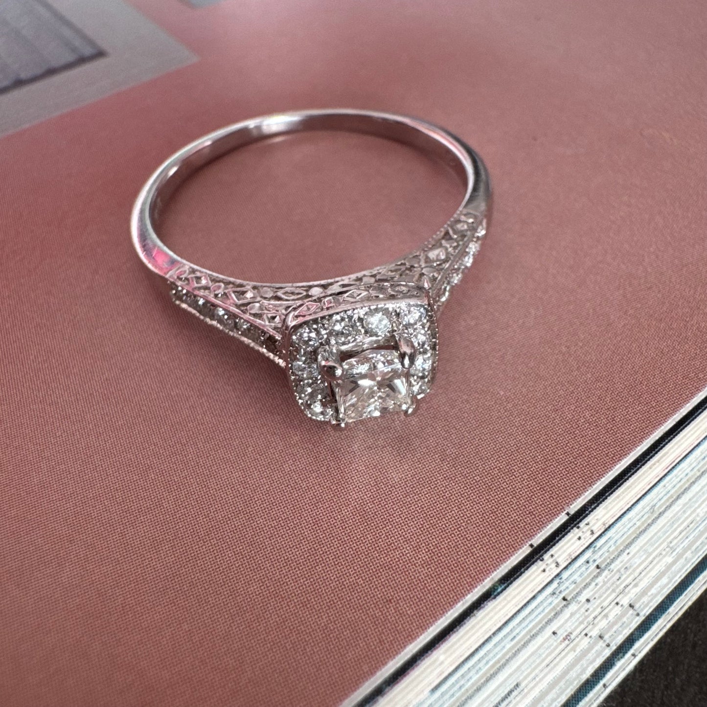 טבעת זהב לבן 14 קראט משובצת יהלום מרכזי בחיתוך פרינסס, מוקף הילת יהלומים קטנים וזרוע משובצת פאווה