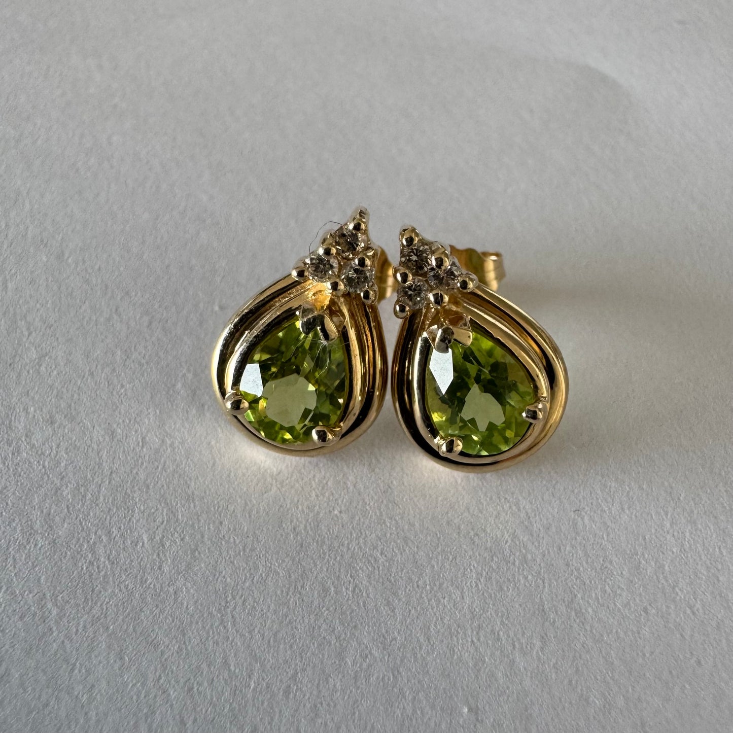 עגילי זהב צהוב 14 קראט משובצים אבני פרידוט בחיתוך טיפה, בגוון ירוק רענן ובוהק. 