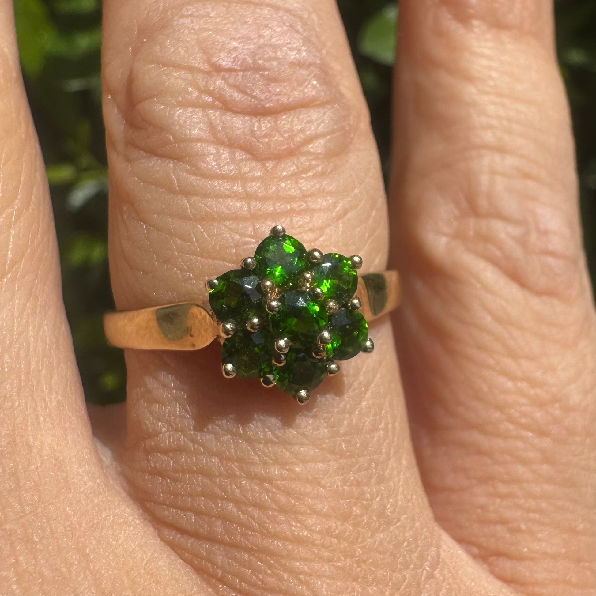 טבעת זהב צהוב 10 קראט משובצת באבני חן ירוקות נוצצות מסודרות בצורת פרח עדין.