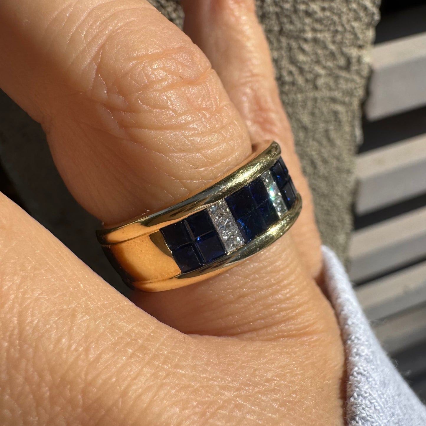 טבעת ה.שטרן זהב צהוב 18 קראט, בעיצוב רחב ומרשים. משובצת שורת אבני ספיר כחולות מרובעות בשילוב מחיצות של יהלומים לנגיעת ברק יוקרתי.