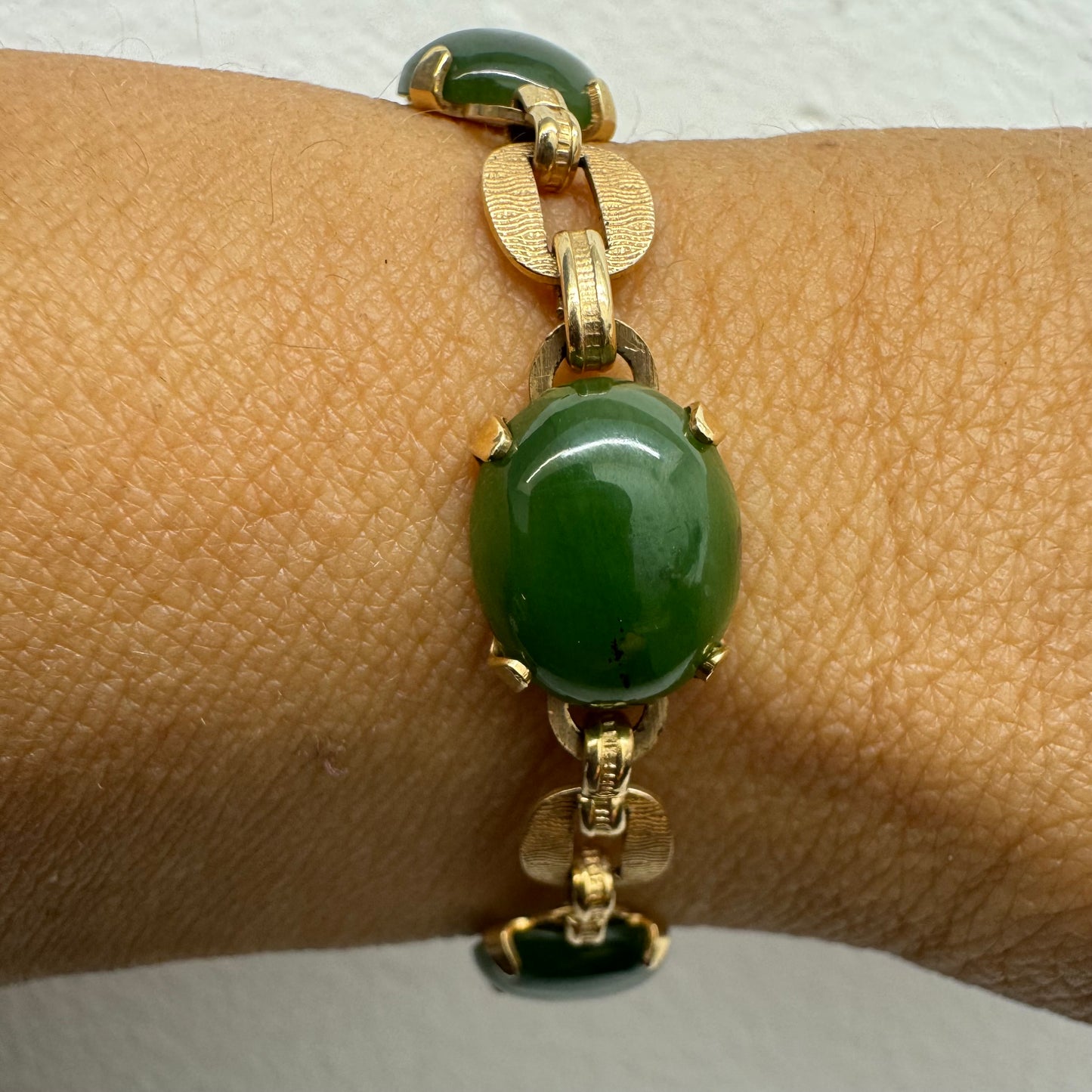 צמיד זהב צהוב 14 קראט משובץ באבני ג’ייד ירוקות בחיתוך קבושון (cabochon) בעיצוב אליפטי, המחוברות ביניהן בחוליות זהב עם טקסטורה מעניינת.