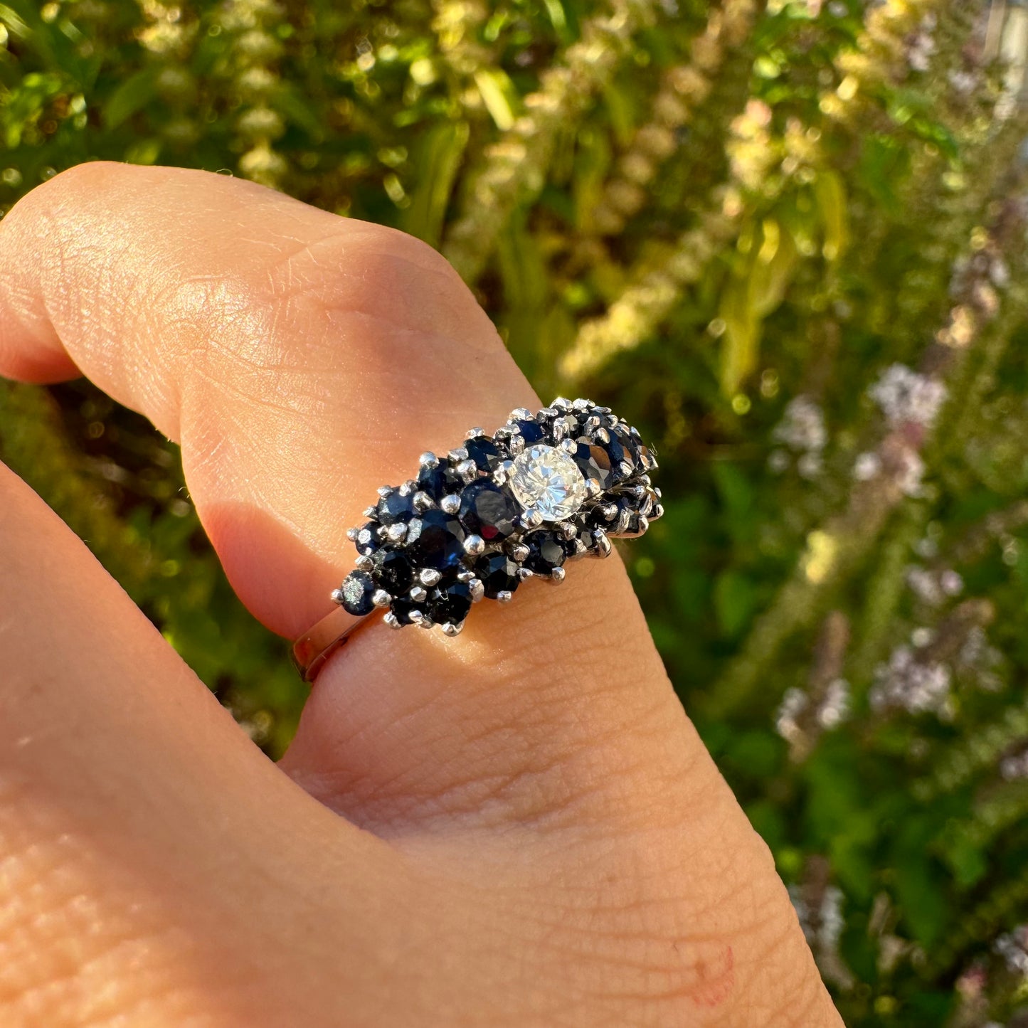 18K gold ring set with a brilliant-cut central Diamond, surrounded by a striking cluster of deep blue Sapphires.