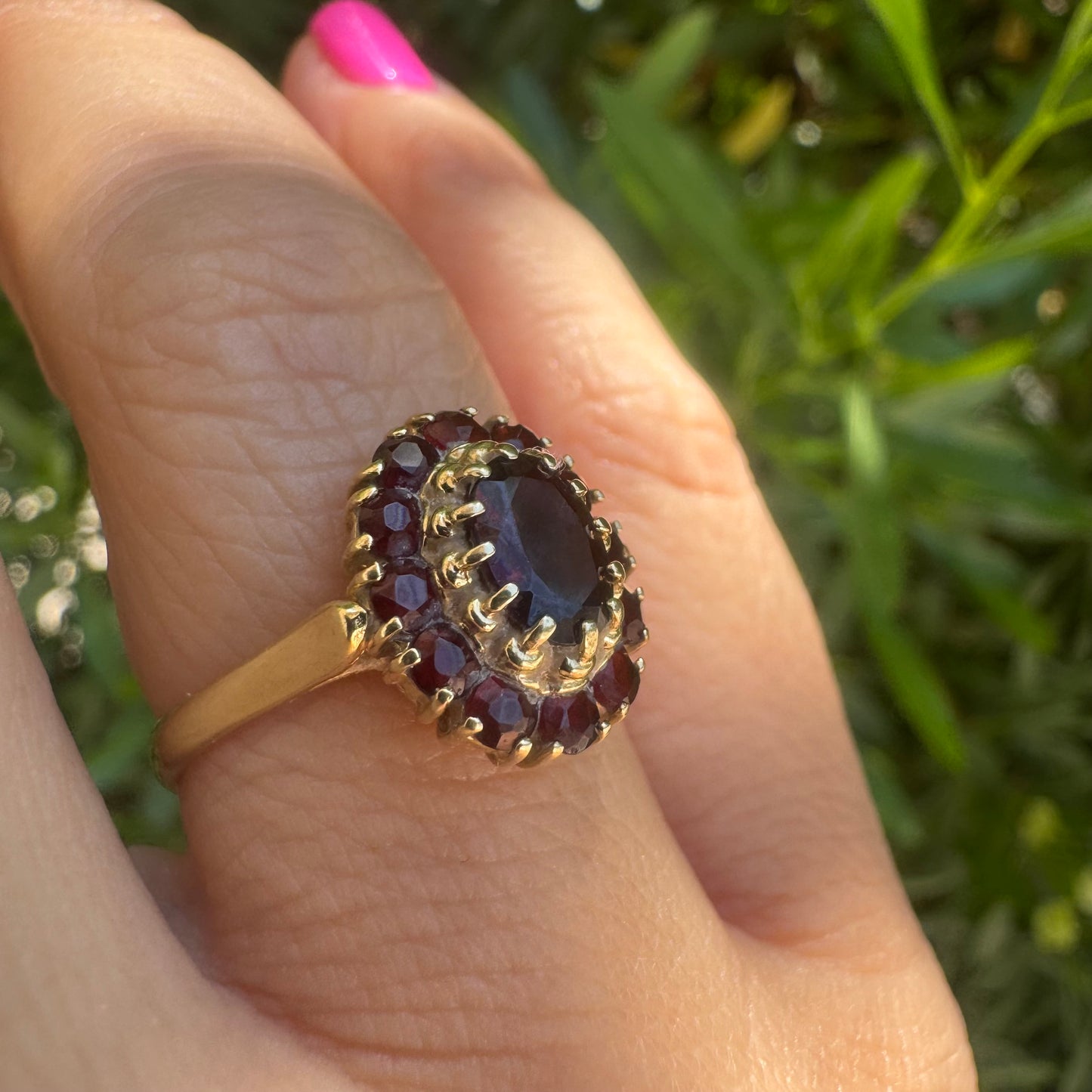 18K gold ring set with an oval garnet center stone, surrounded by smaller garnets