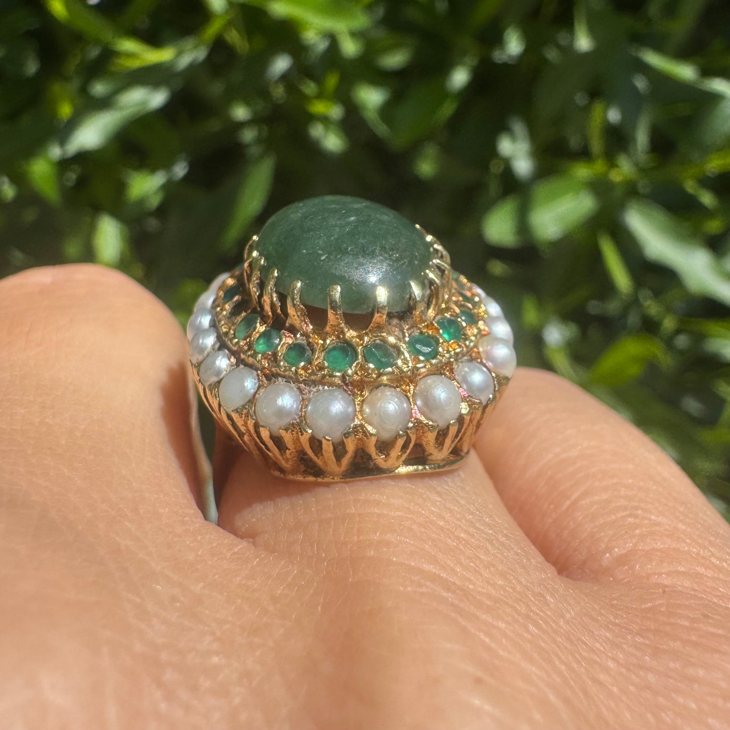14K gold set with a large oval green Jade at its center, surrounded by concentric halos of sparkling Emeralds and delicate pearls