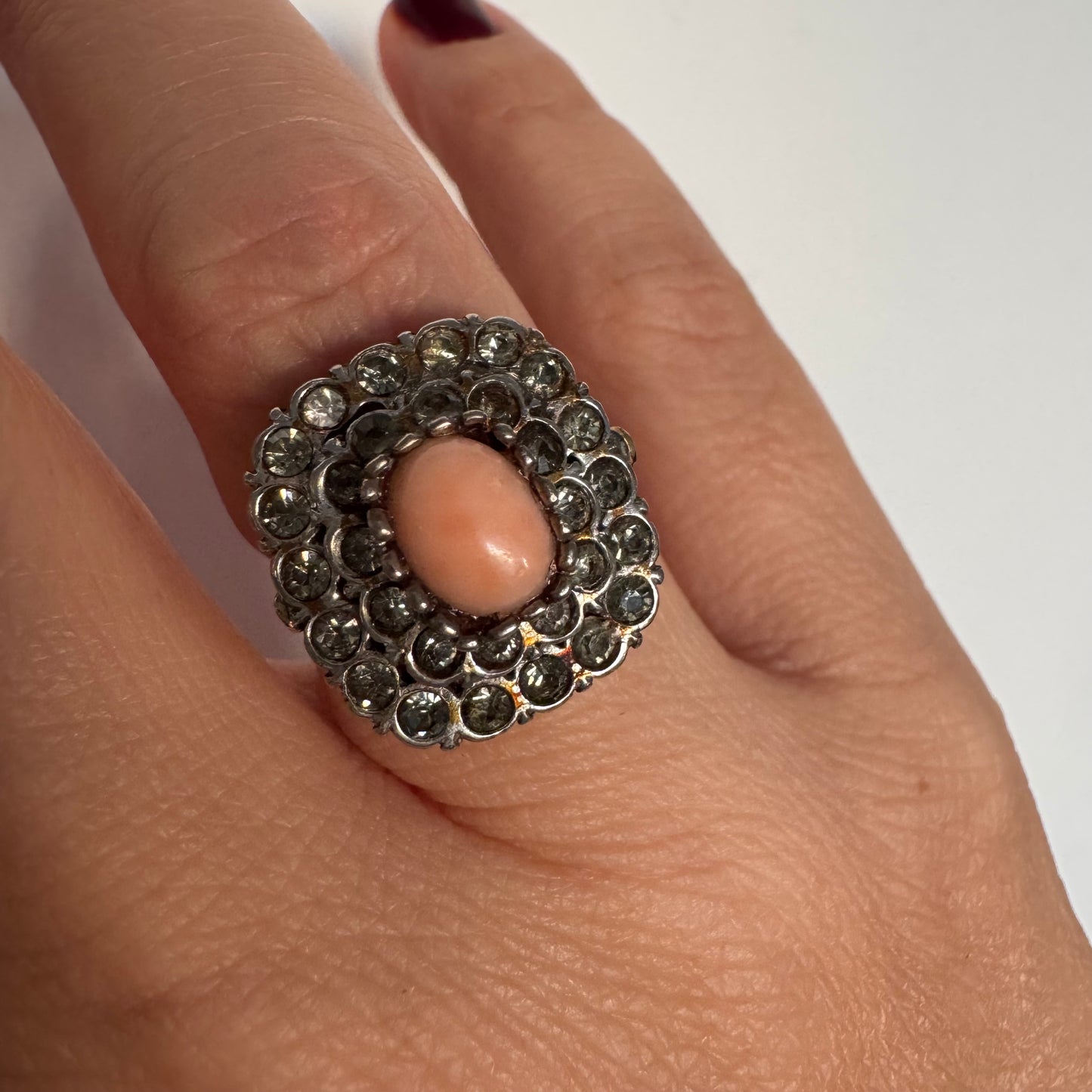 טבעת וינטג׳ עם חלק תחתון מזהב 14 קראט וחלק עליון עשוי כסף משובצת אבן קורל בהירה במרכז ומסביבה אבנים בהירות שאינן יהלומים.