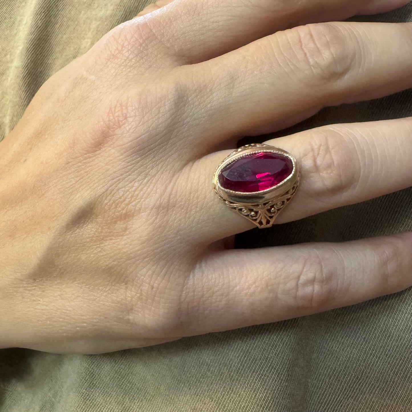 14K gold ring crowned with a vivid oval-cut Ruby, framed in an ornate bezel and accented by intricate filigree details