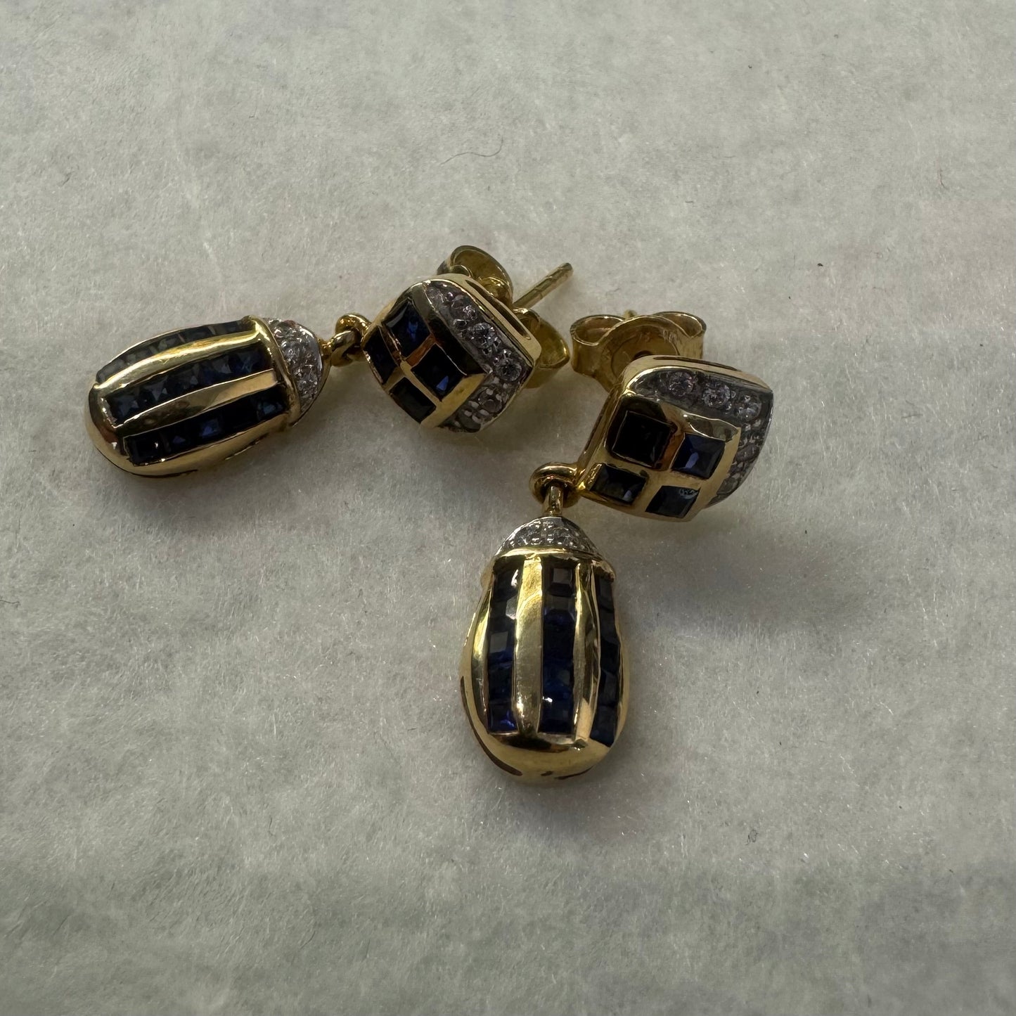 עגילי זהב צהוב 18 קראט תלויים, משובצים אבני ספיר כחולות בגוון כחול עמוק בעיצוב גיאומטרי, בשילוב יהלומים מנצנצים