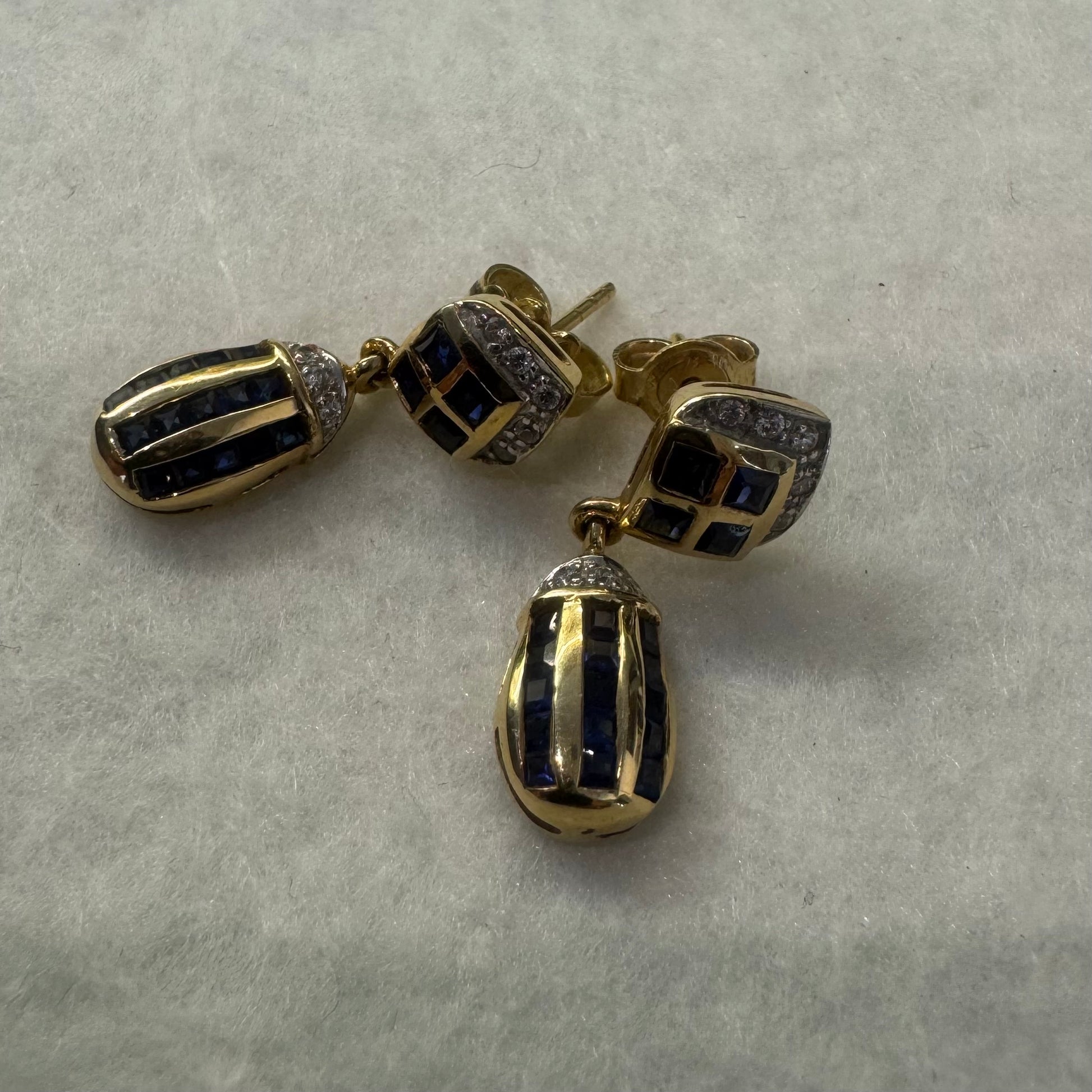 עגילי זהב צהוב 18 קראט תלויים, משובצים אבני ספיר כחולות בגוון כחול עמוק בעיצוב גיאומטרי, בשילוב יהלומים מנצנצים