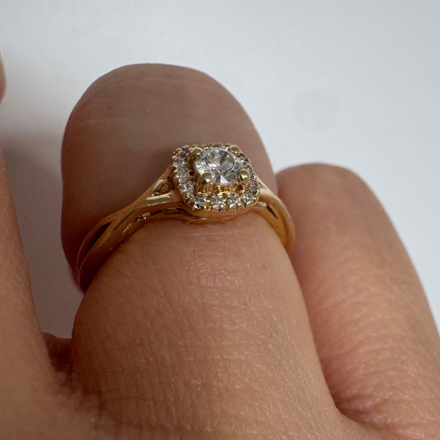 טבעת זהב 14 קראט משובצת יהלום מרכזי עגול ומבריק, מוקף הילה עדינה של יהלומים המעצימים את הברק