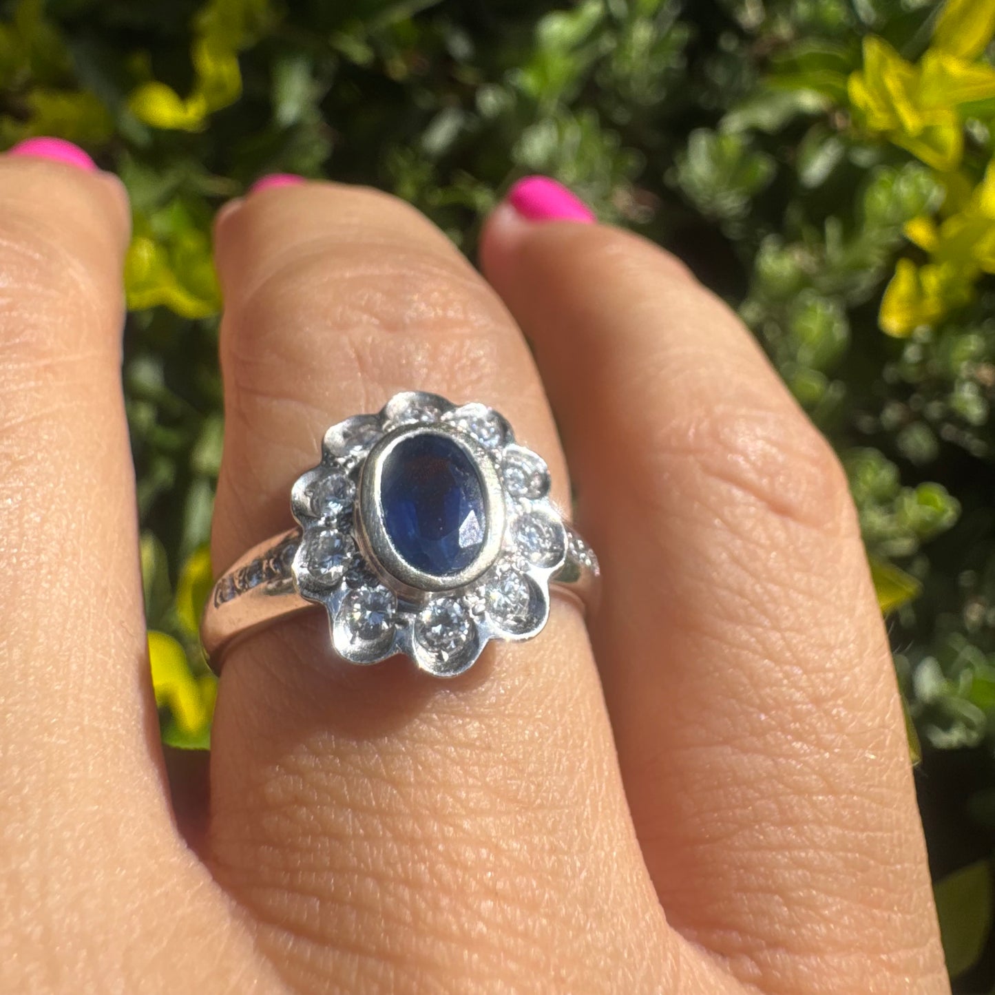 18K gold ring set with an oval blue Sapphire surrounded by a halo of round Diamonds in a flower-shaped design.