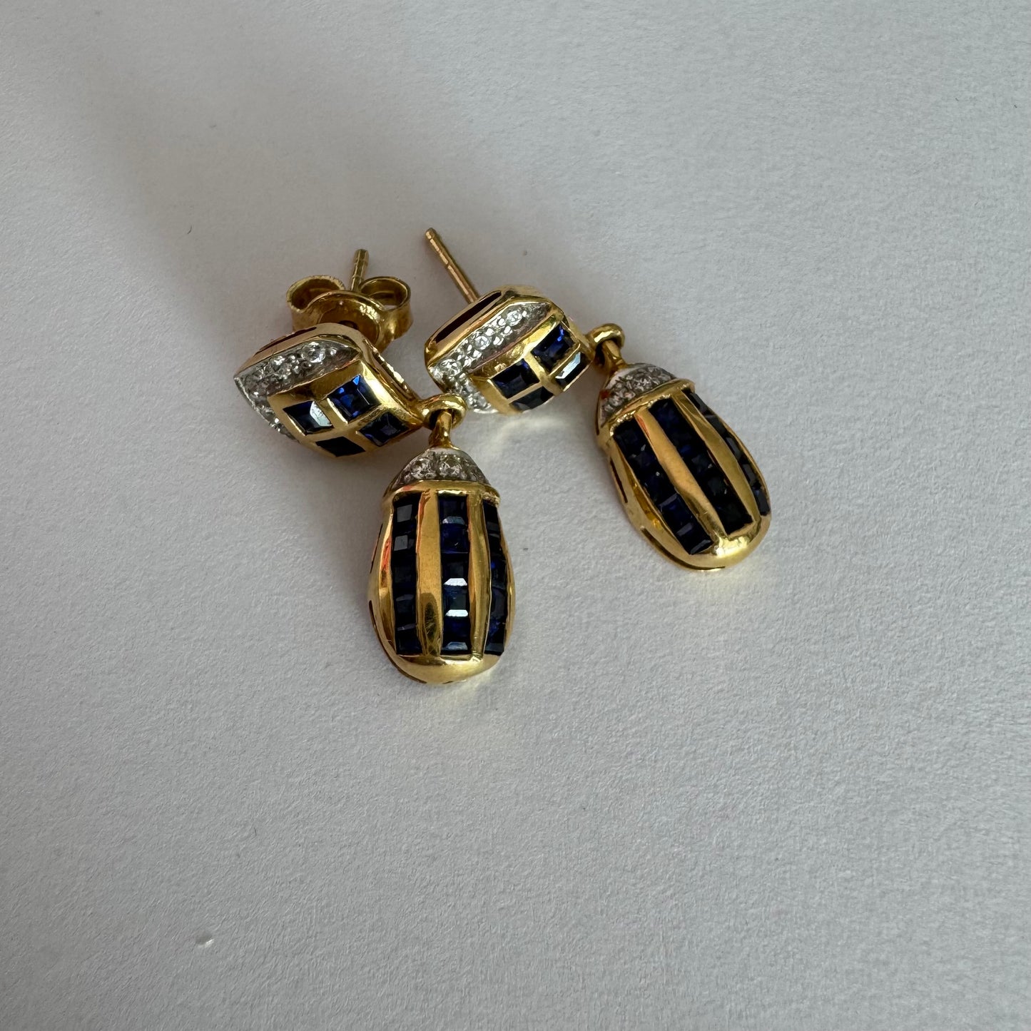 עגילי זהב צהוב 18 קראט תלויים, משובצים אבני ספיר כחולות בגוון כחול עמוק בעיצוב גיאומטרי, בשילוב יהלומים מנצנצים