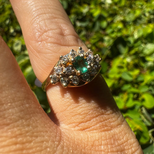 14K gold ring set with Emerald at its center, surrounded by a halo of brilliant-cut diamonds arranged in a floral-inspired cluster