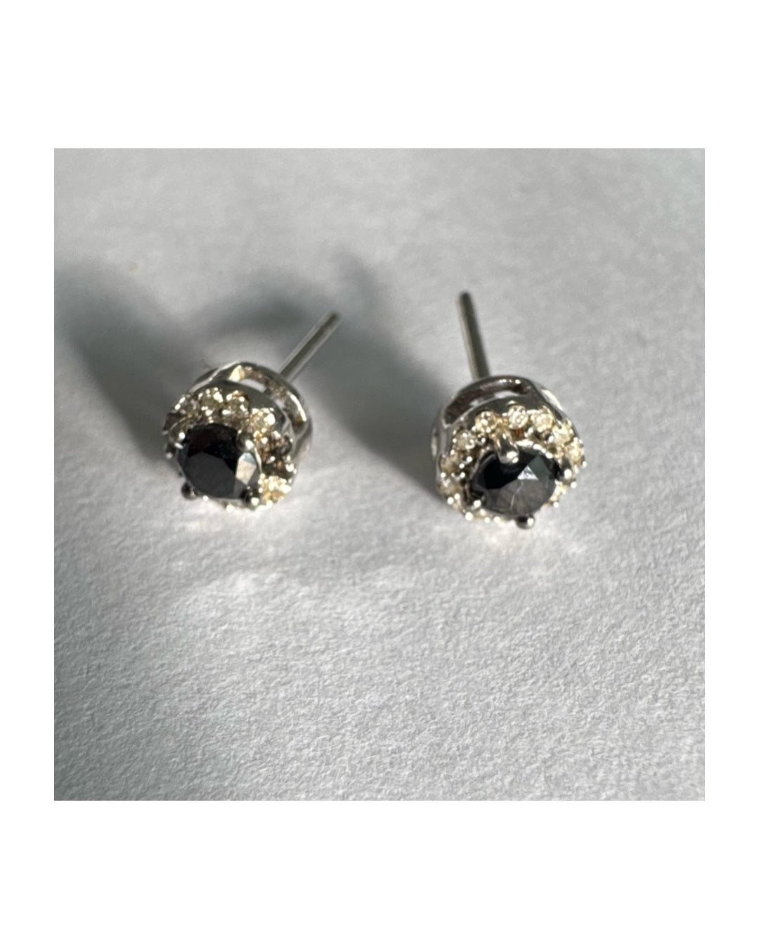 עגילי זהב לבן 10 קראט צמודים לאוזן, משובצים יהלומים שחורים עגולים במרכז ומסביבם הילה של יהלומים לבנים מנצנצים.