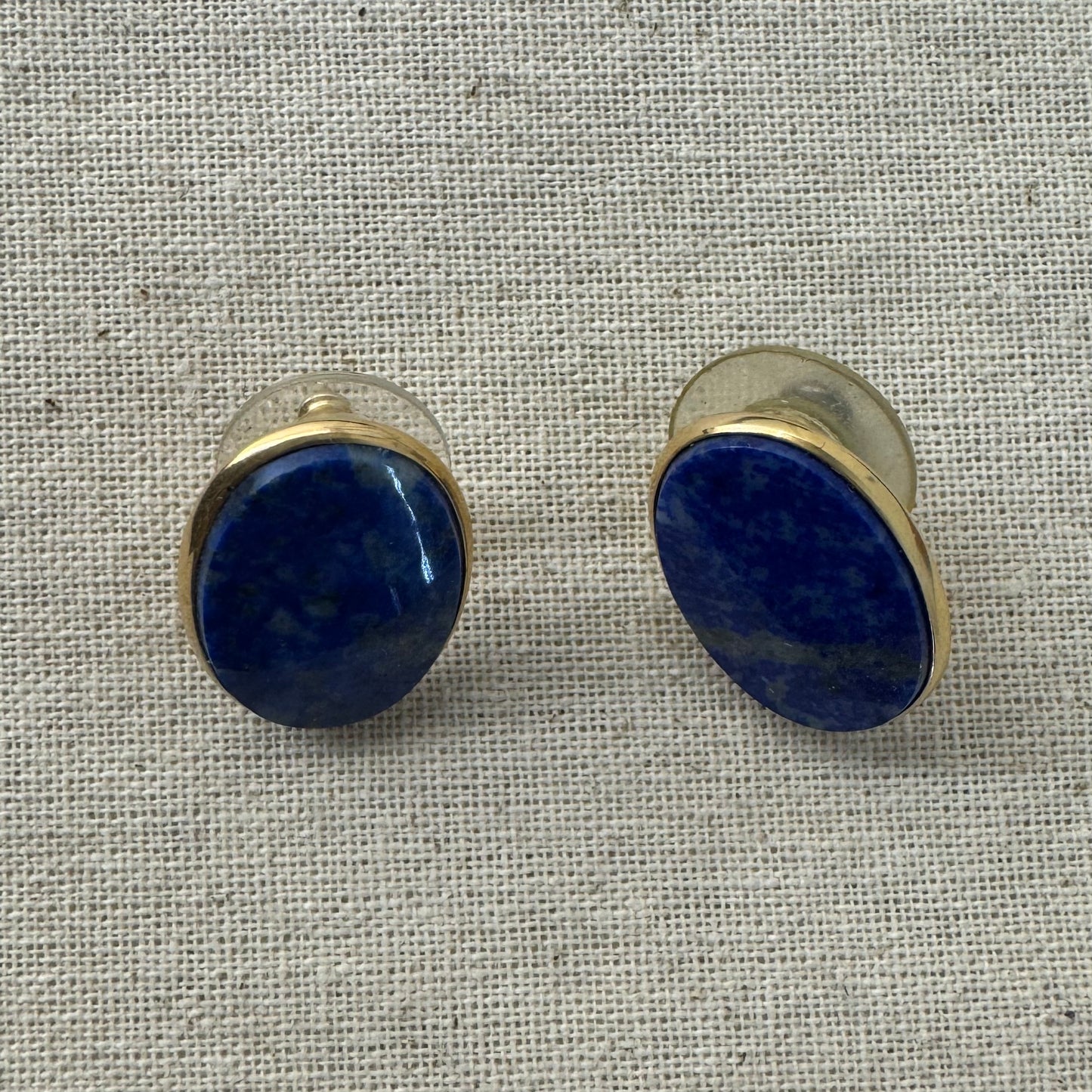14K gold stud earrings set with polished oval Lapis Lazuli stones in a sleek gold bezel setting.