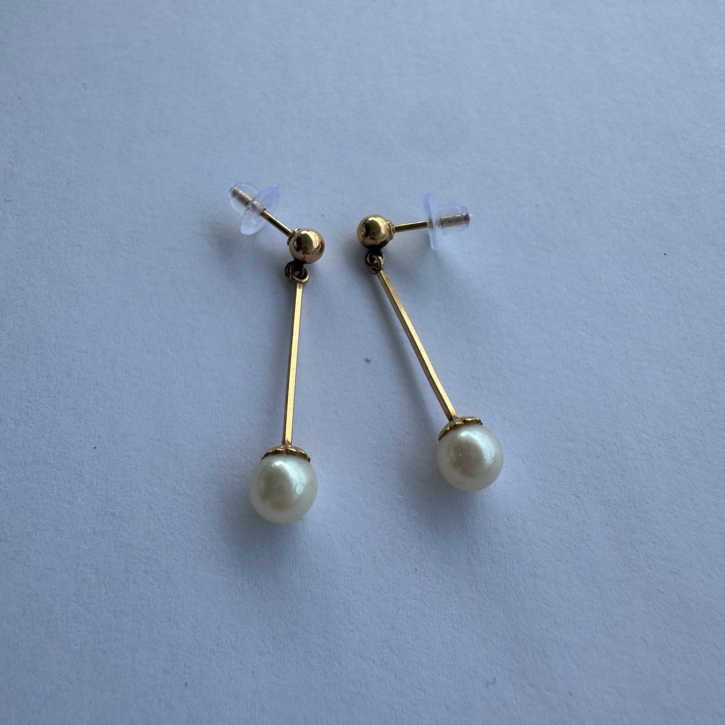 עגילי זהב 14 קראט בעיצוב תלוי ועדין, עם פנינה עגולה בקצה.