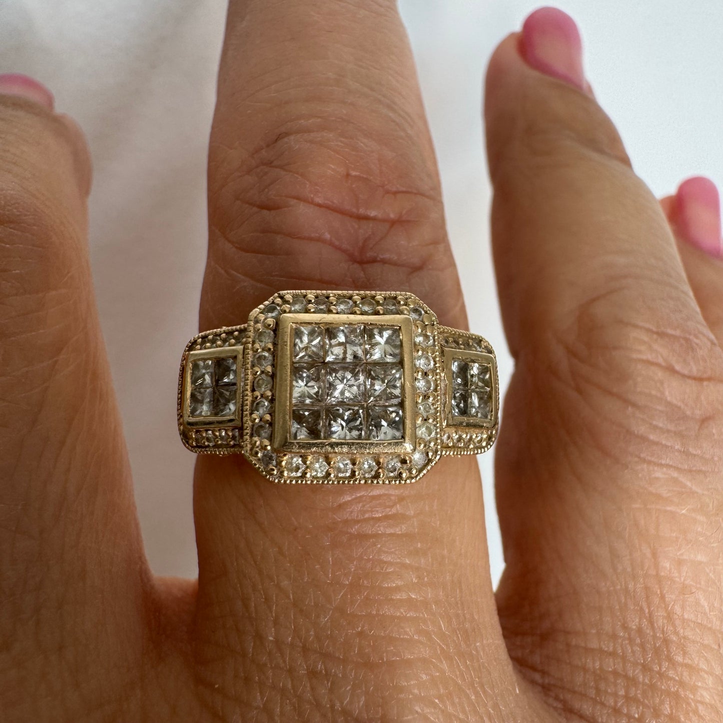 טבעת זהב צהוב 14 קראט משובצת יהלומים בחיתוך פרינסס במרכז, מוקפת הילה של יהלומים צדדיים.