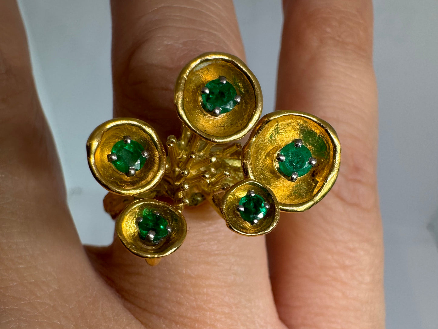 18K gold ring with an artistic floral-inspired design, set with round Emerald in textured circular settings.