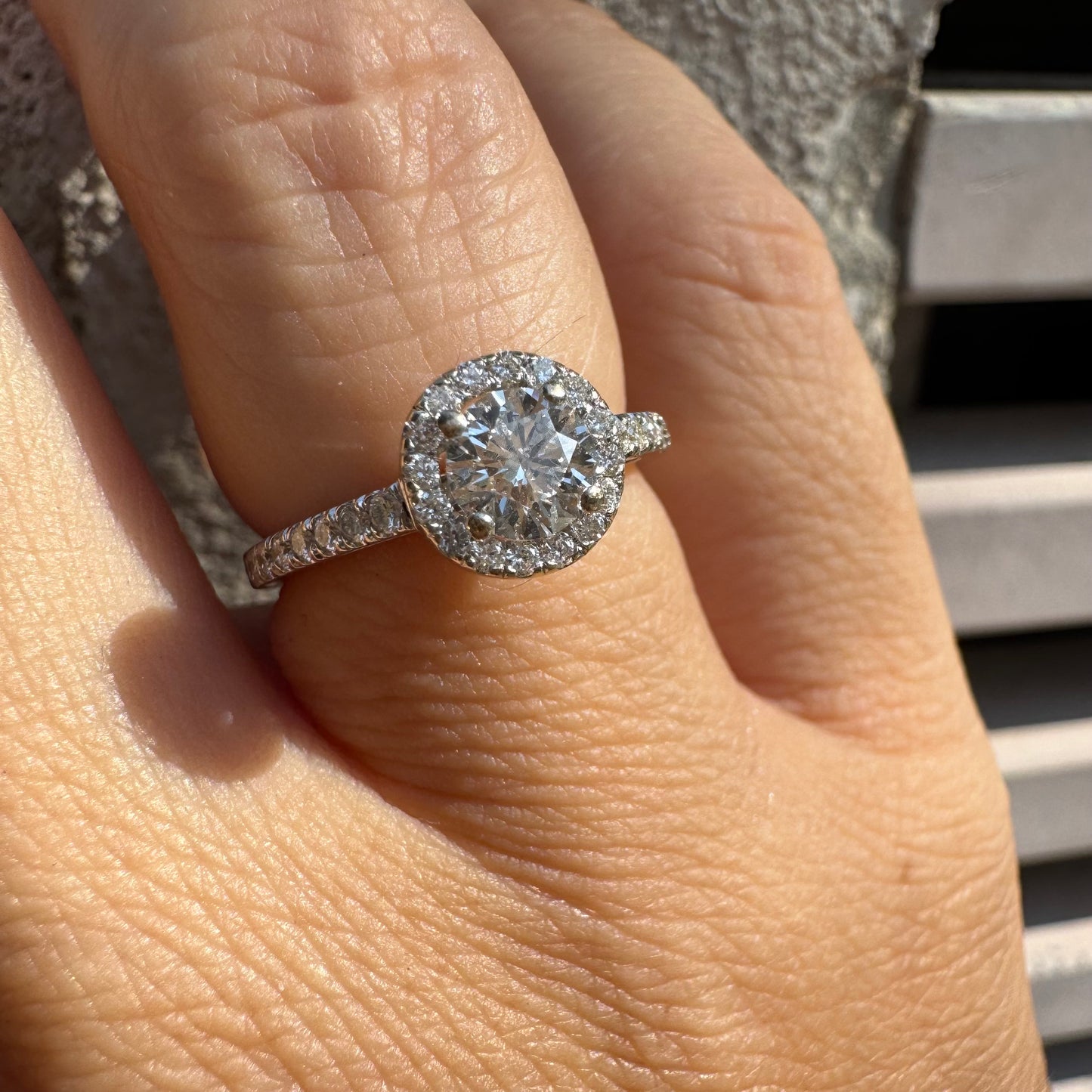 טבעת זהב לבן 14 קראט משובצת יהלום מרכזי עגול והילה נוצצת של יהלומים קטנים, עם יהלומים נוספים על החישוק.