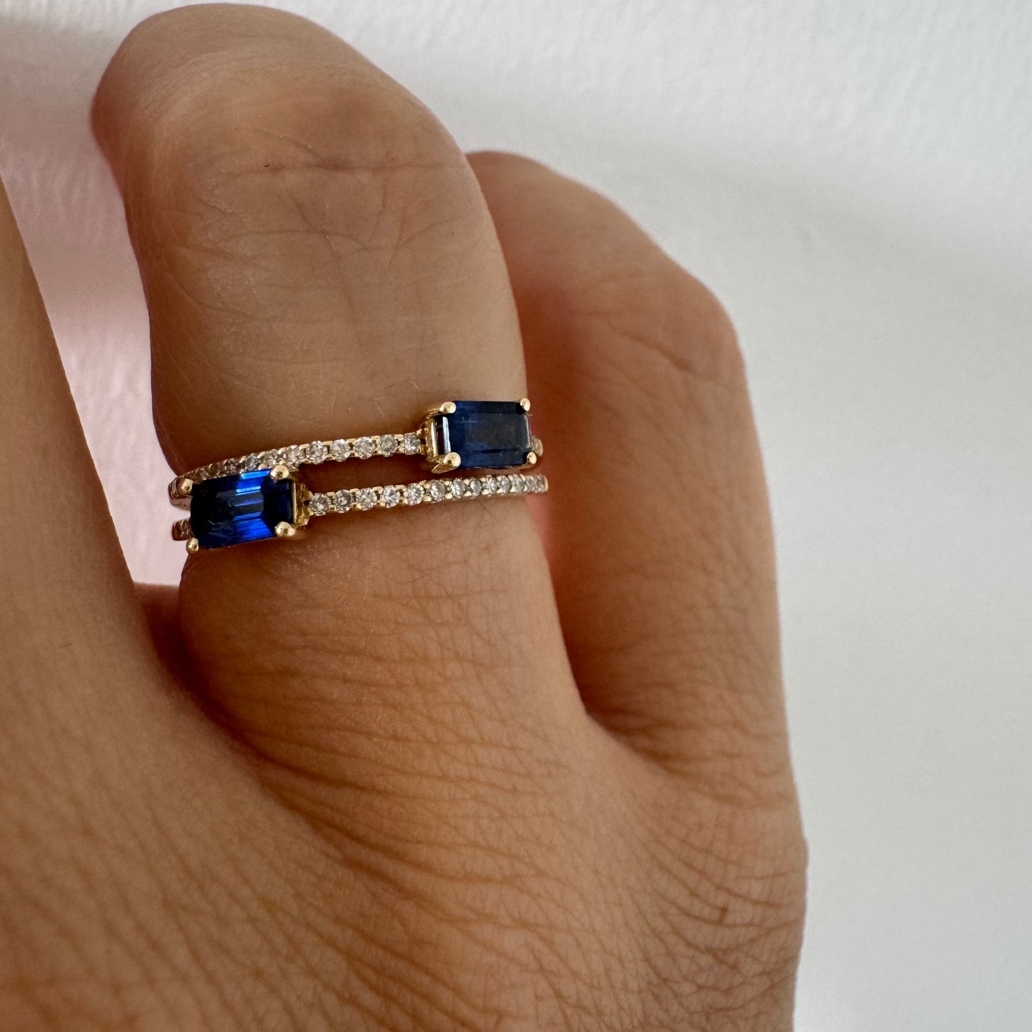 טבעת זהב צהוב 14 קראט בעיצוב פתוח, משובצת שתי אבני ספיר בחיתוך אמרלד ושורות יהלומים עדינים.