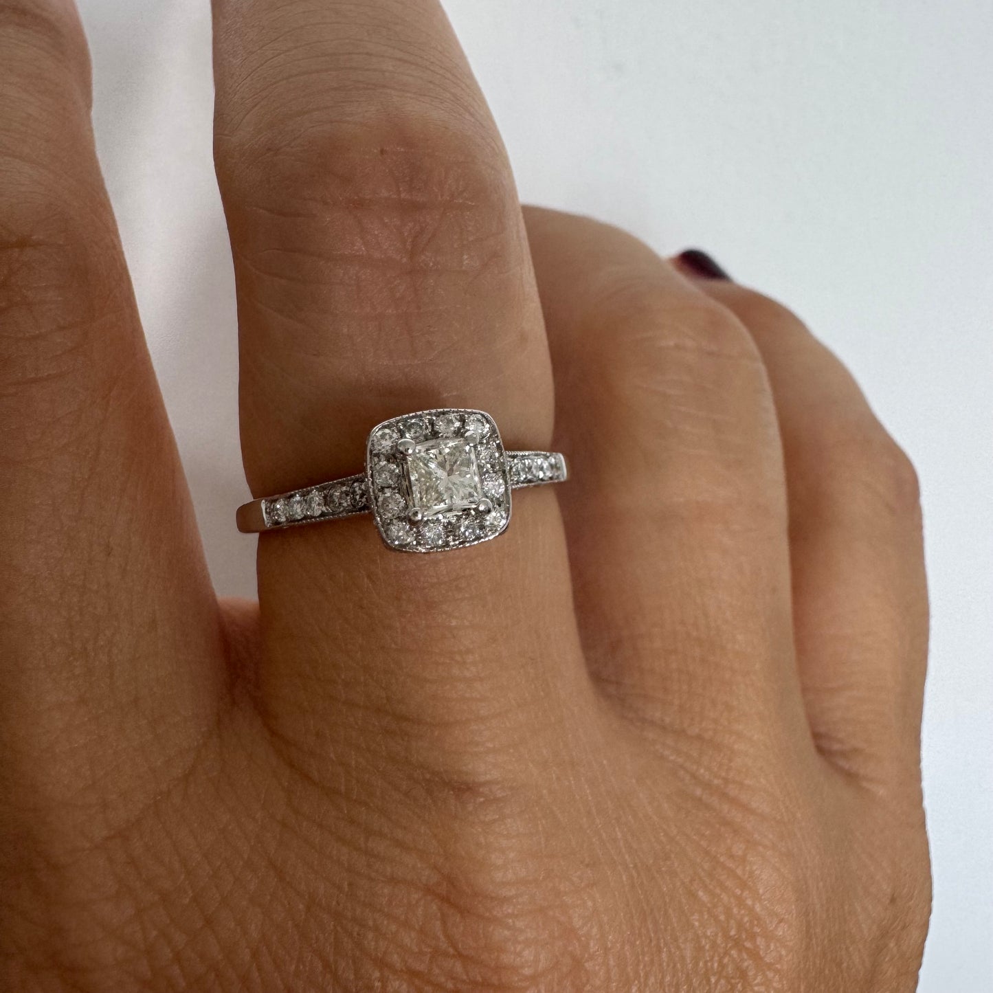 טבעת זהב לבן 14 קראט משובצת יהלום מרכזי בחיתוך פרינסס, מוקף הילת יהלומים קטנים וזרוע משובצת פאווה