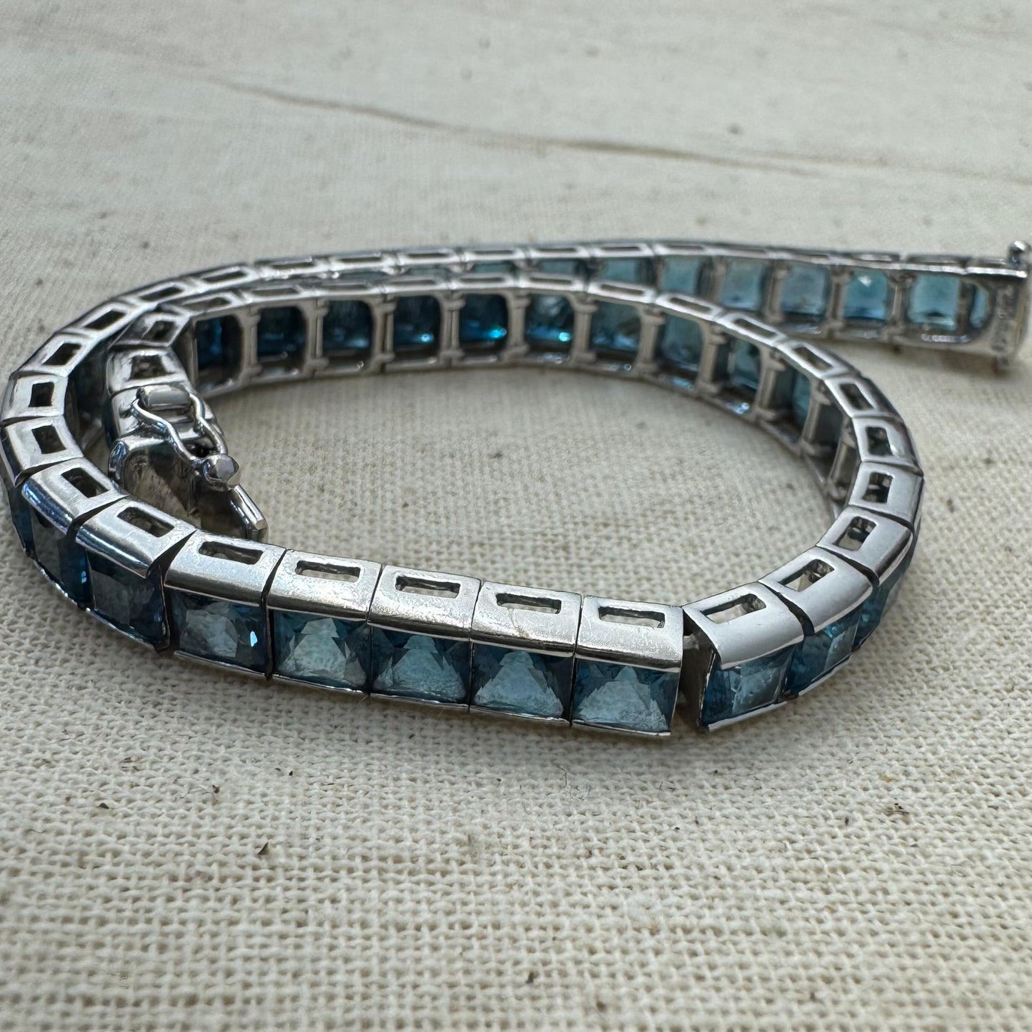 צמיד זהב לבן 18 קראט של המותג ה.שטרן משובץ אבני טופז כחולה&nbsp;בשיבוץ ערוץ חלק וקלאסי – פריט נצחי עם טאץ’ מודרני