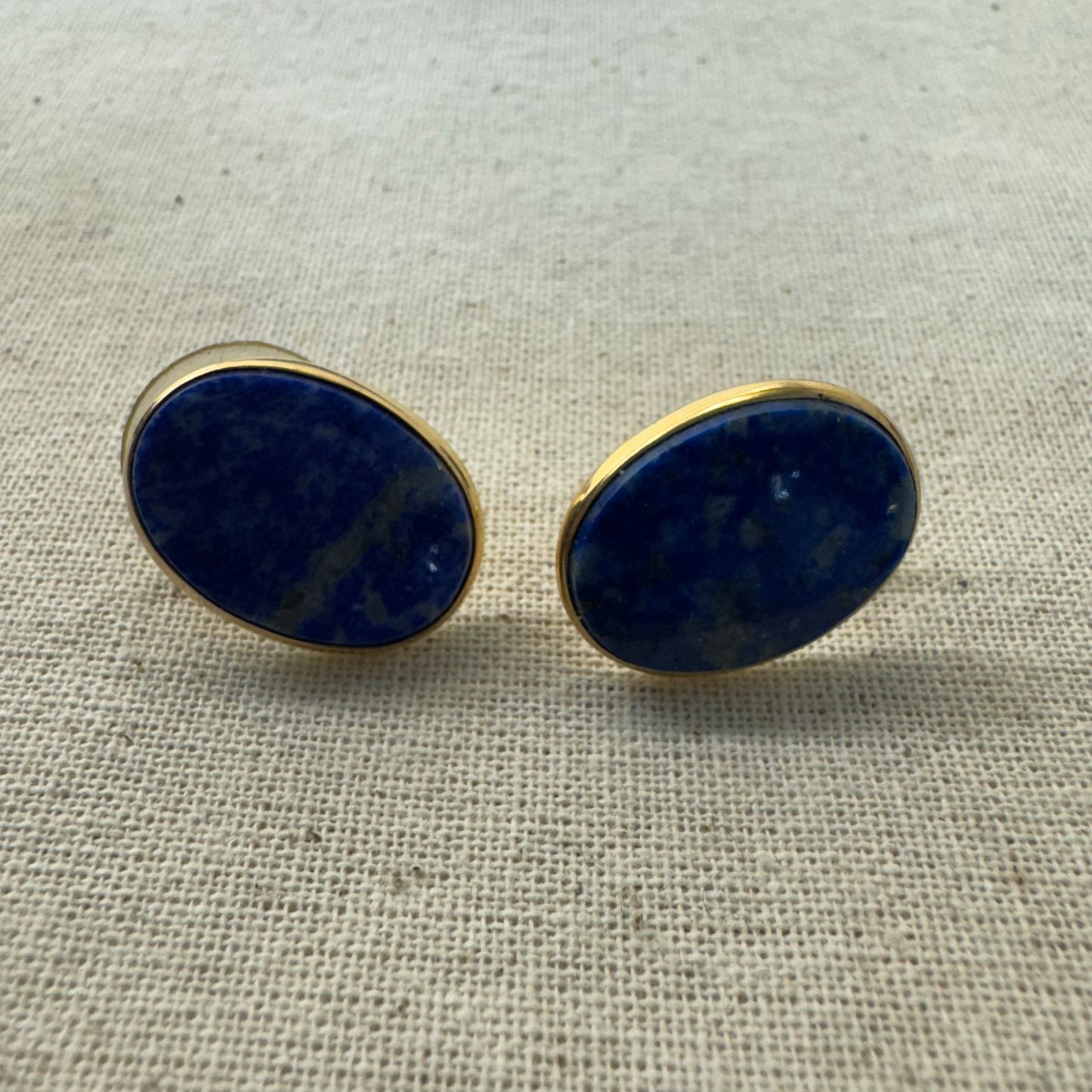 14K gold stud earrings set with polished oval Lapis Lazuli stones in a sleek gold bezel setting.