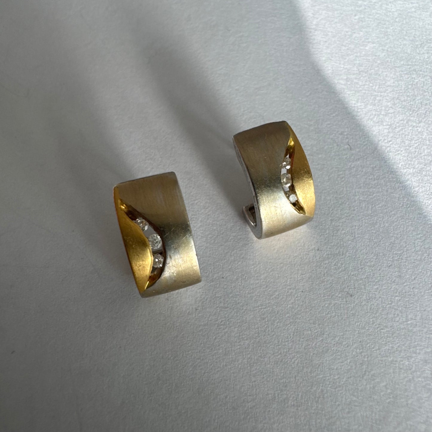 עגילי זהב 18 קראט משובצים יהלומים בעיצוב מודרני ונקי עם שילוב של שני גוונים וגימור מאט יוקרתי.