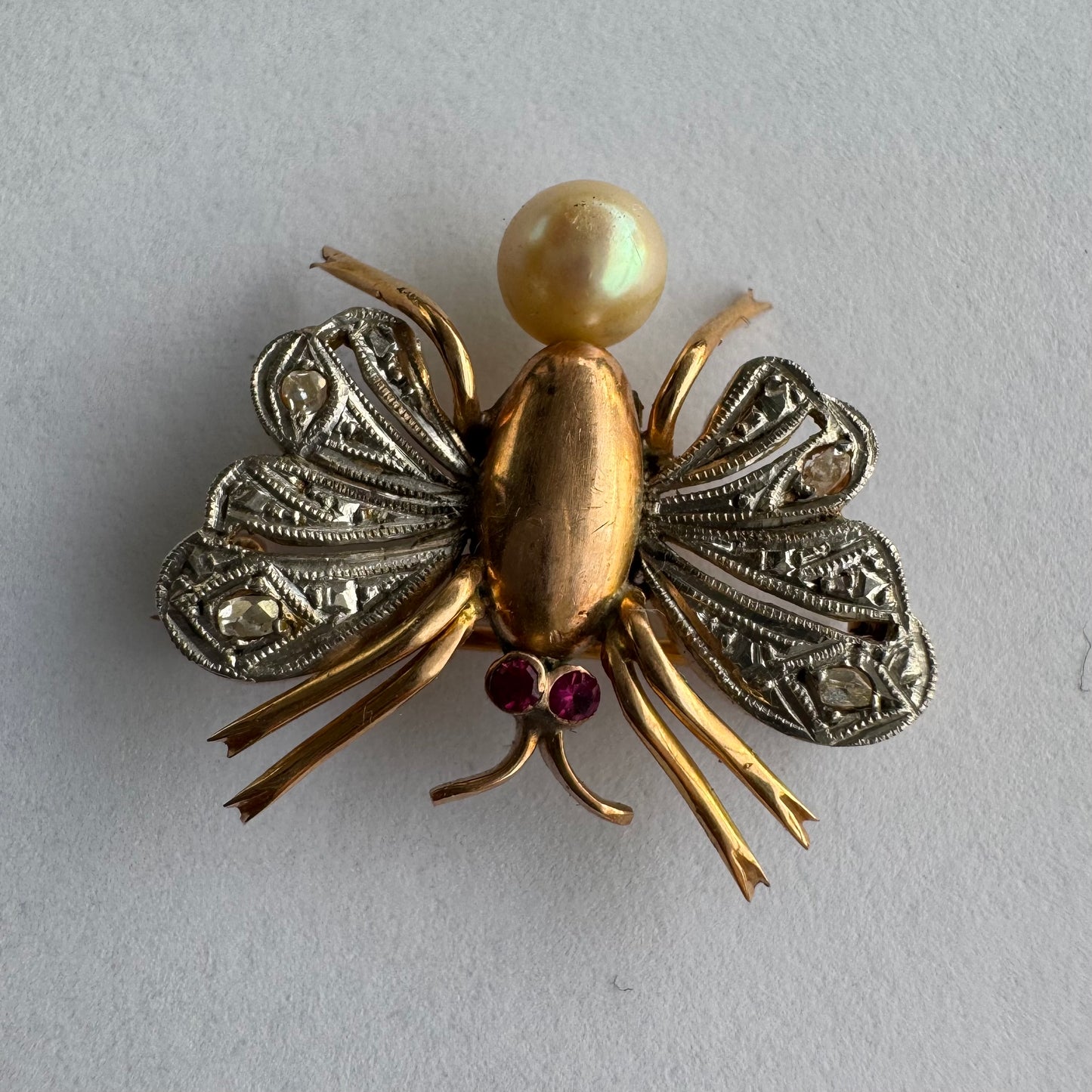 סיכת חרק ייחודית עשויה זהב 14 קראט משובצת יהלומים בעבודת פיליגרן עדינה בכנפיים, אבני רובי אדומות בעיניים ופנינה טבעית בגוון שמפניה.