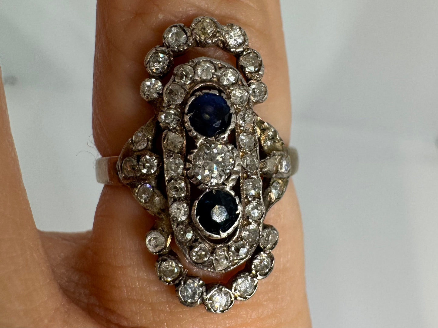 14K gold Antique featuring a stunning trio of gemstones - two deep blue Sapphires surrounding a brilliant old-cut Diamonds