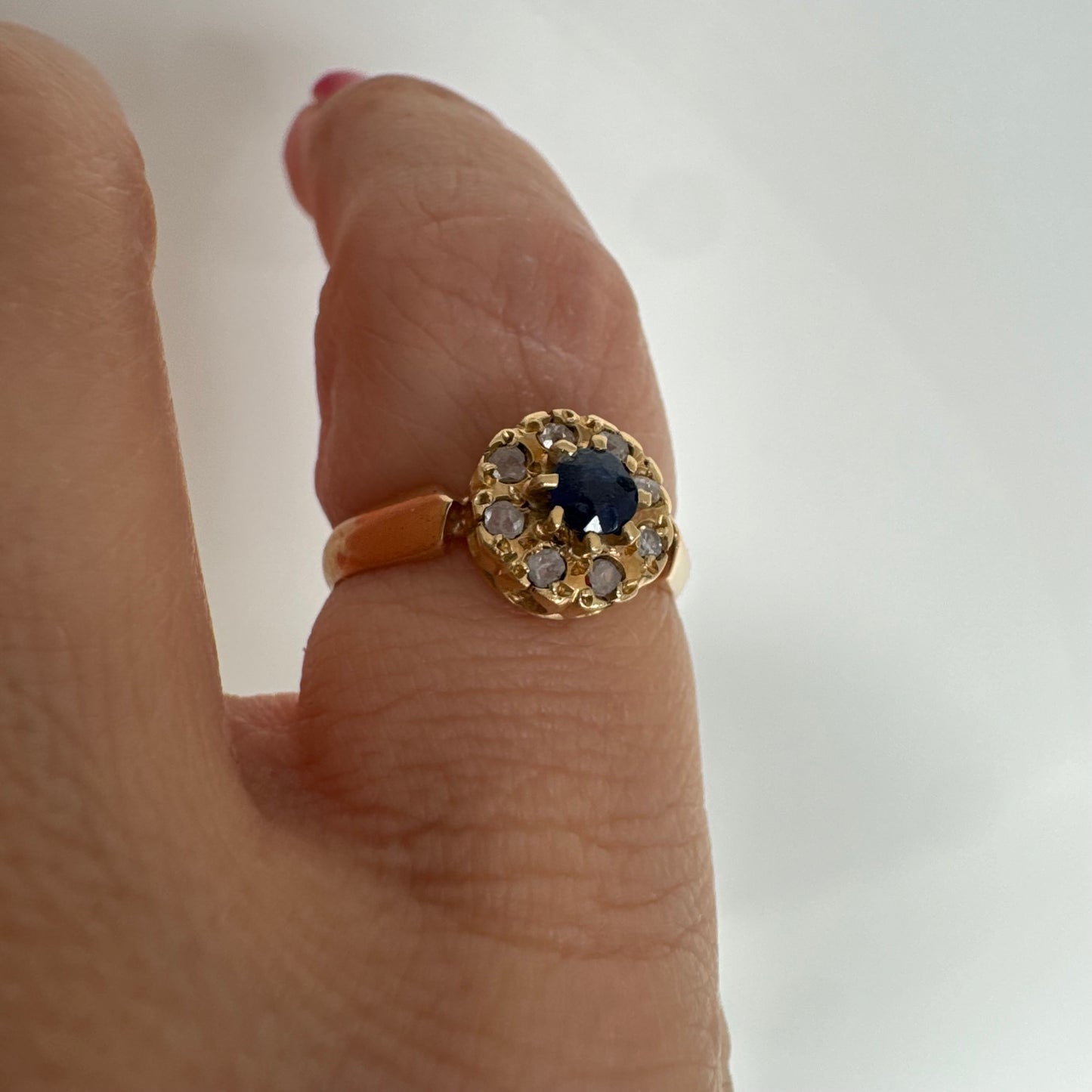 טבעת זהב 14 קראט משובצת ספיר מרכזי מוקף הילה של יהלומים בחיתוך עגול.