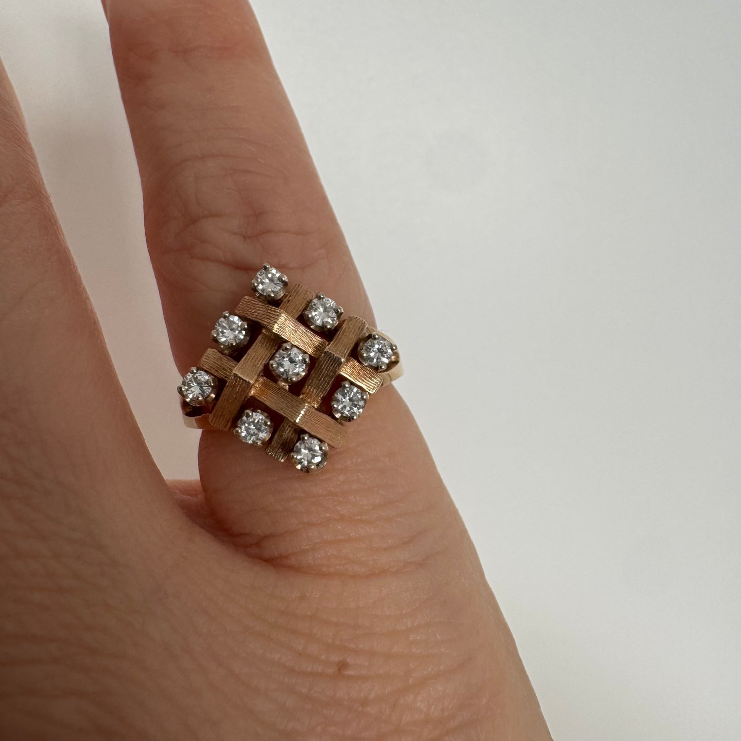 טבעת זהב צהוב 14 קראט בעיצוב קלוע וגאומטרי, משובצת יהלומים עגולים בפריסה סימטרית.