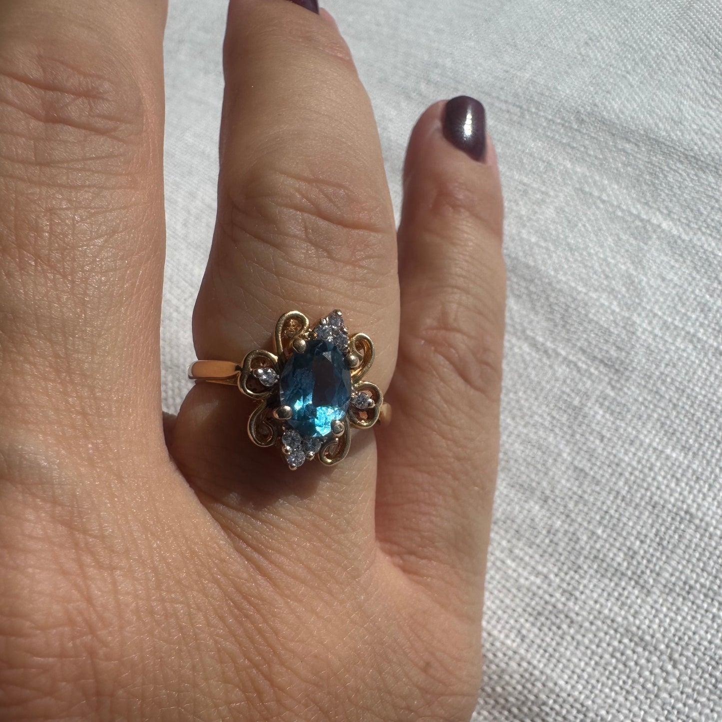 18K gold ring featuring an oval-cut Blue Topaz at the center, accented by sparkling side Diamonds and elegant scroll details.