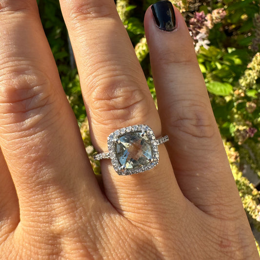 טבעת זהב לבן 14 קראט משובצת באבן אקוומרין בגוון תכלת ומוקפת במסגרת כפולה של יהלומים עגולים מנצנצים.