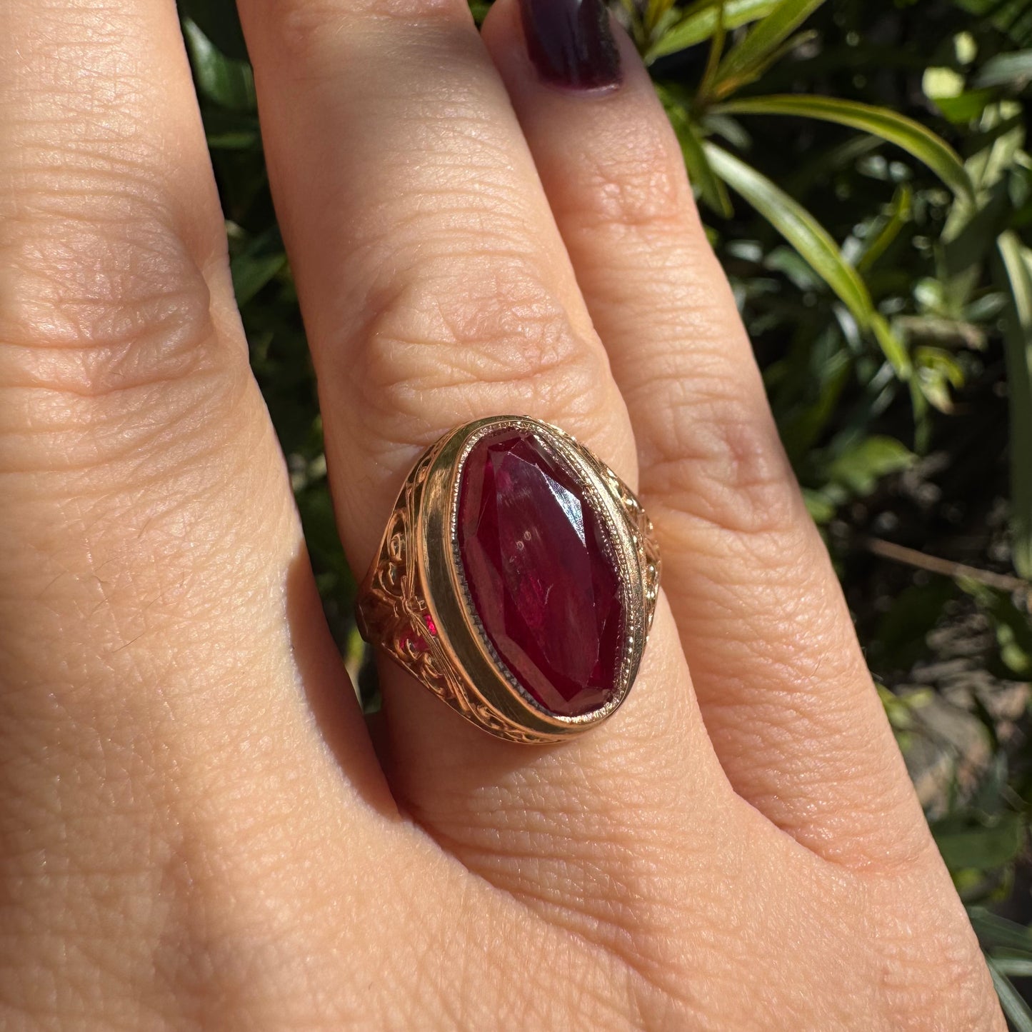 14K gold ring crowned with a vivid oval-cut Ruby, framed in an ornate bezel and accented by intricate filigree details