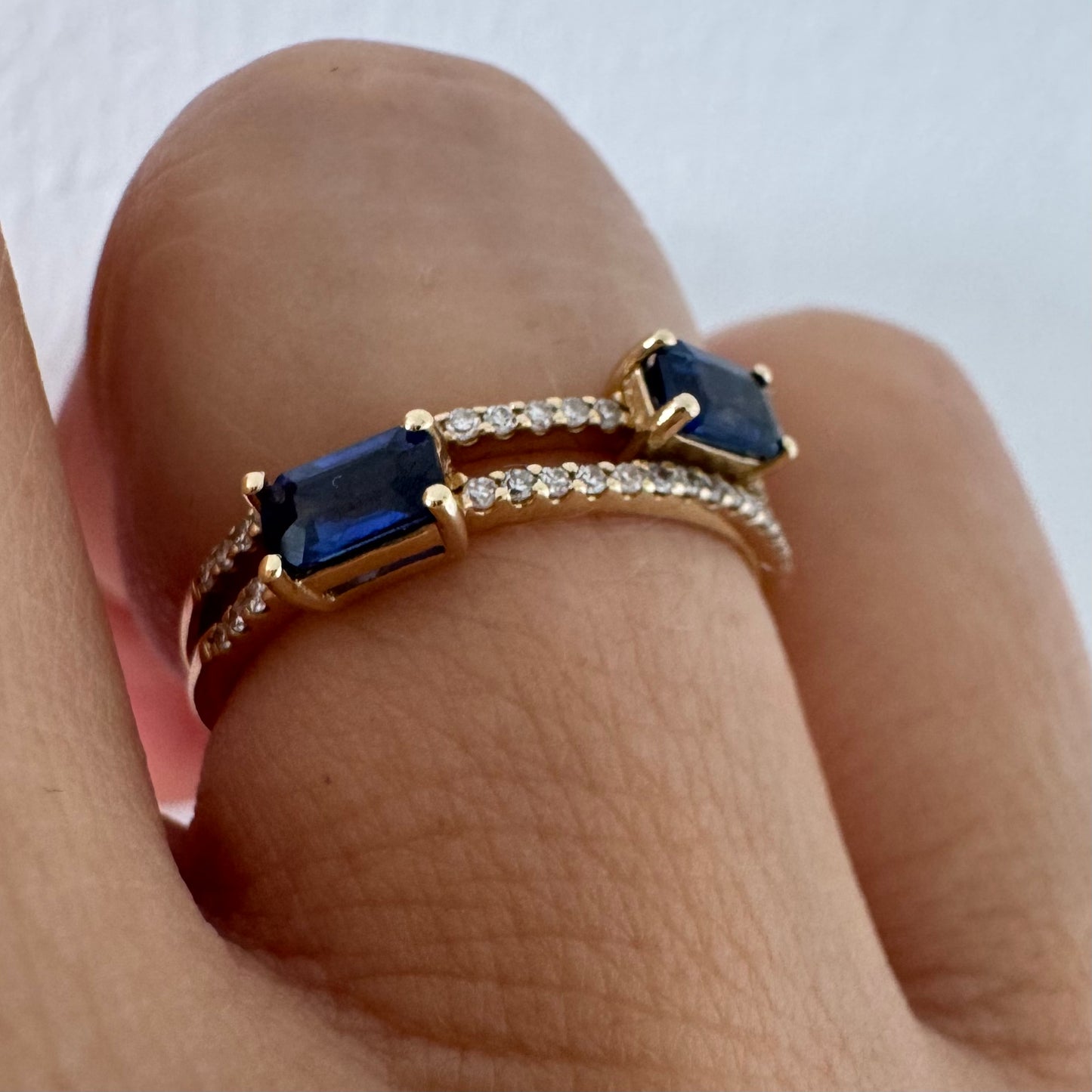 טבעת זהב צהוב 14 קראט בעיצוב פתוח, משובצת שתי אבני ספיר בחיתוך אמרלד ושורות יהלומים עדינים.