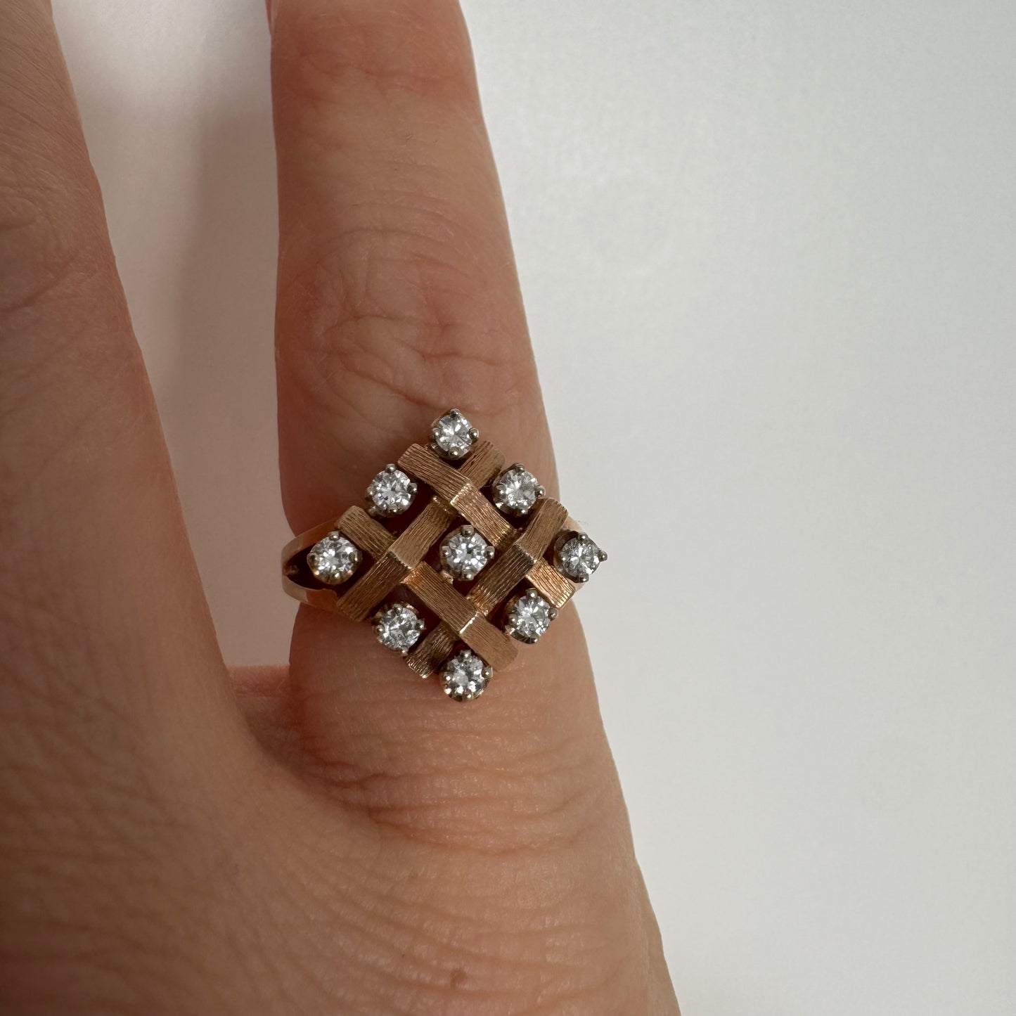 טבעת זהב צהוב 14 קראט בעיצוב קלוע וגאומטרי, משובצת יהלומים עגולים בפריסה סימטרית.