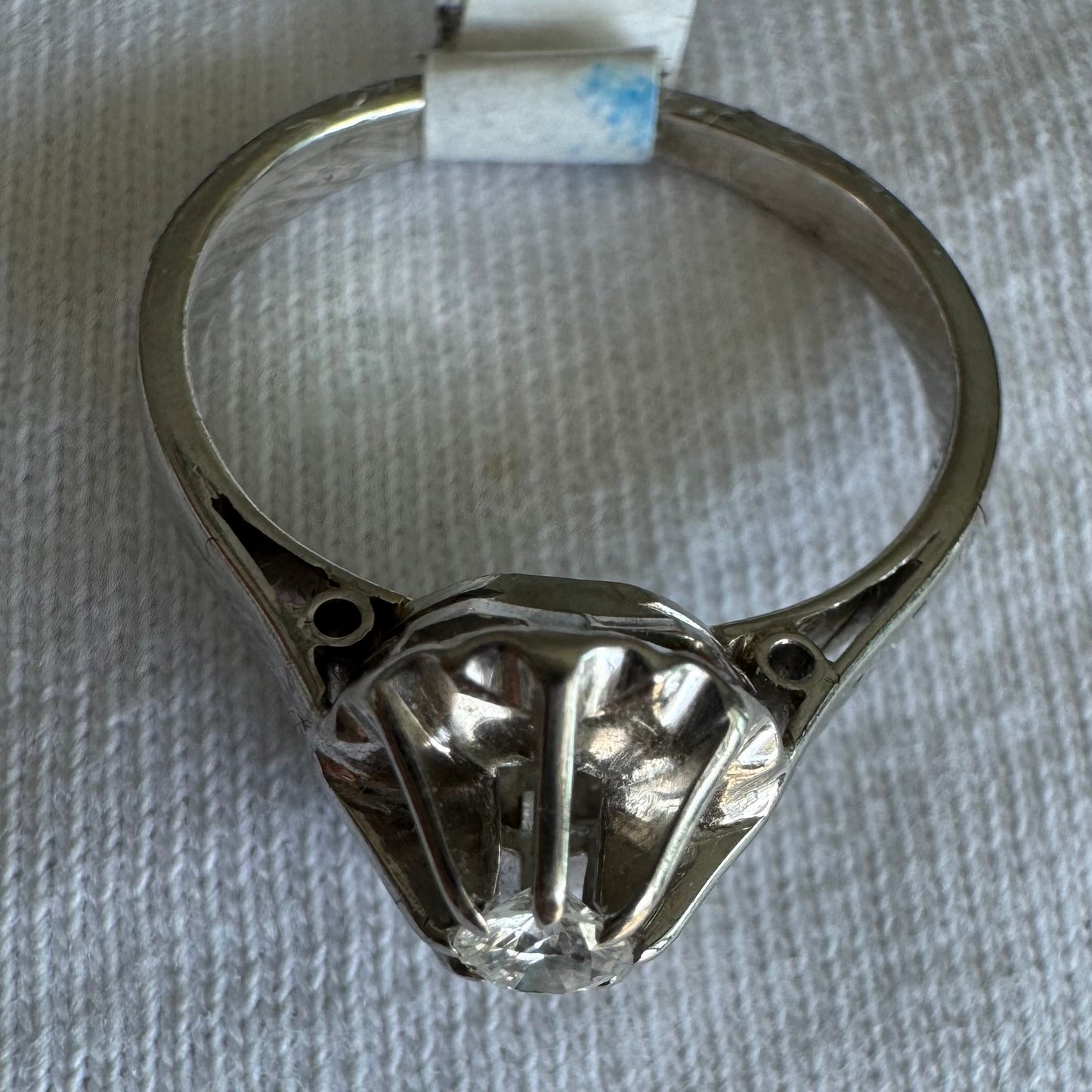 טבעת זהב לבן 18 קראט בעיצוב פיסולי עם יהלום מרכזי בחיתוך מבריק, משובץ במסגרת מחורצת שמשקפת את האור בעוצמה