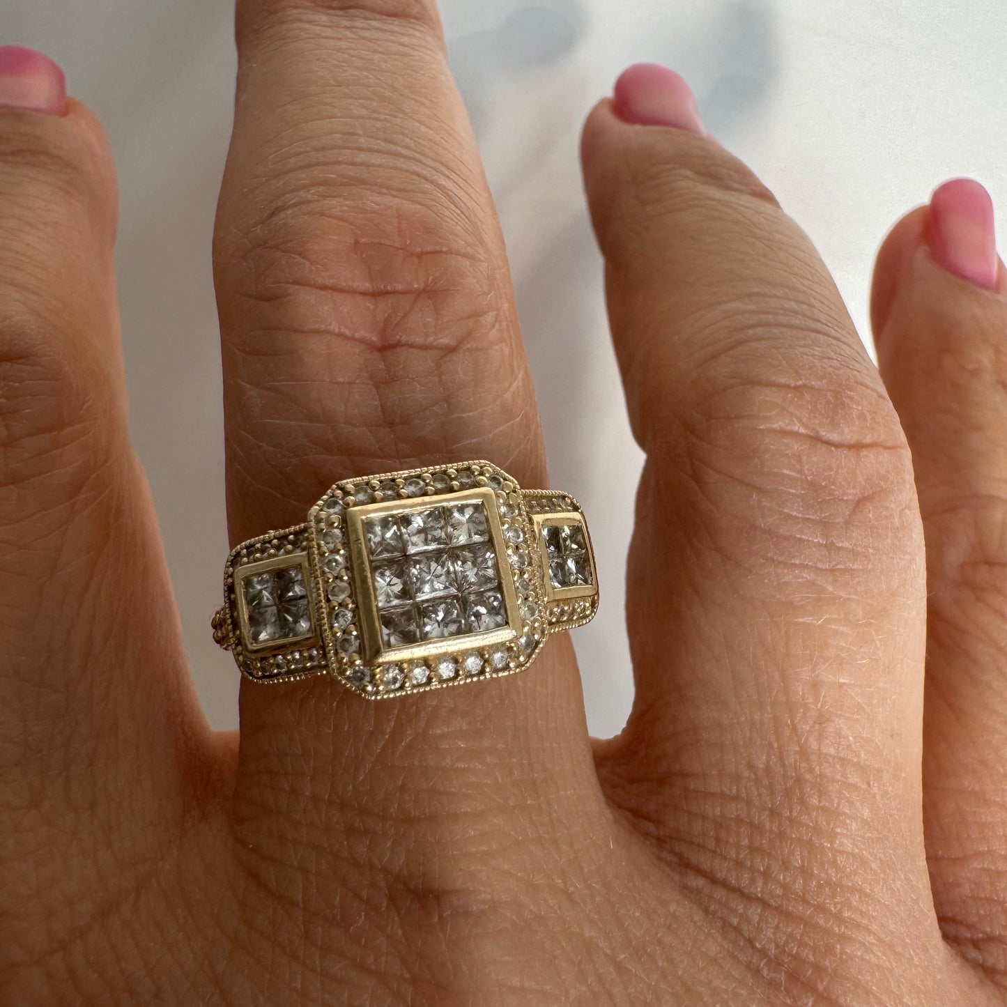 טבעת זהב צהוב 14 קראט משובצת יהלומים בחיתוך פרינסס במרכז, מוקפת הילה של יהלומים צדדיים.