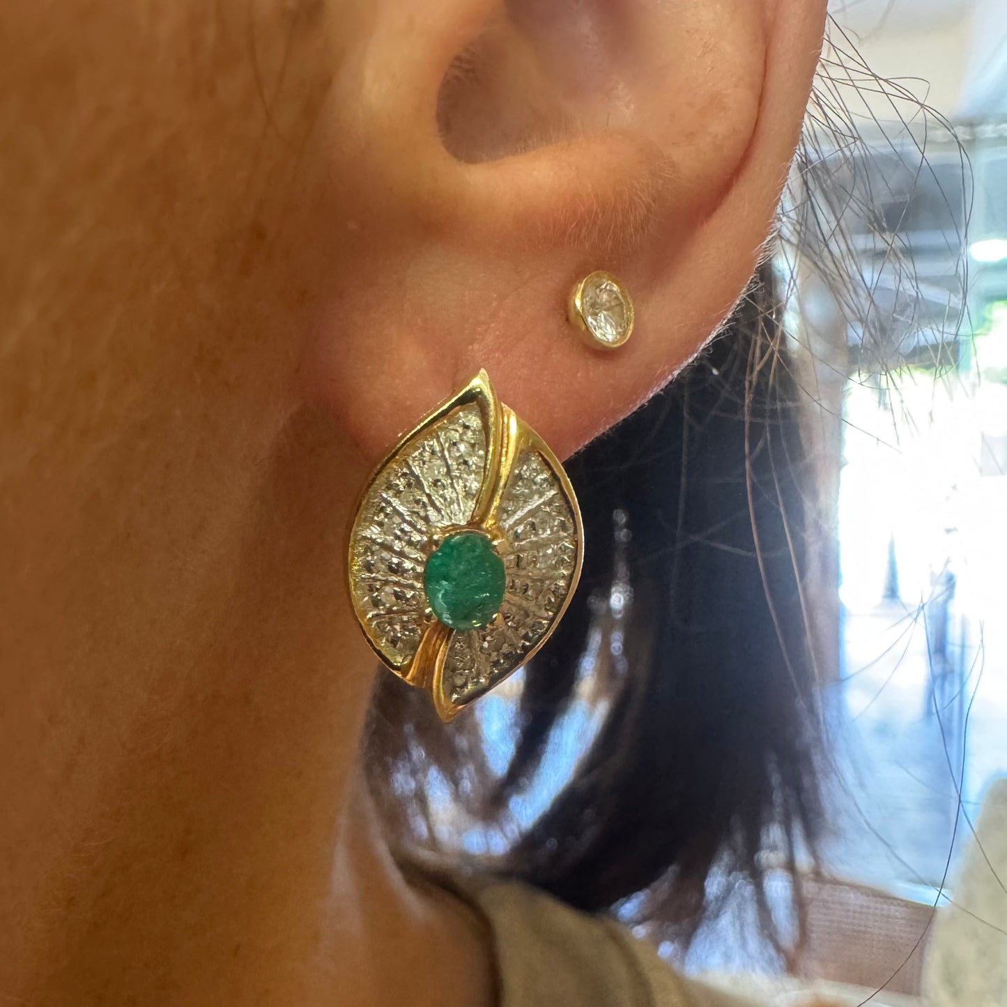 עגילים צמודים לאוזן, זהב צהוב 14 קראט, משובצים אמרלד במרכז, וסביבן פיתוחים משובצים יהלומים, שמעניקים מראה של ניצוץ רך ואלגנטי
