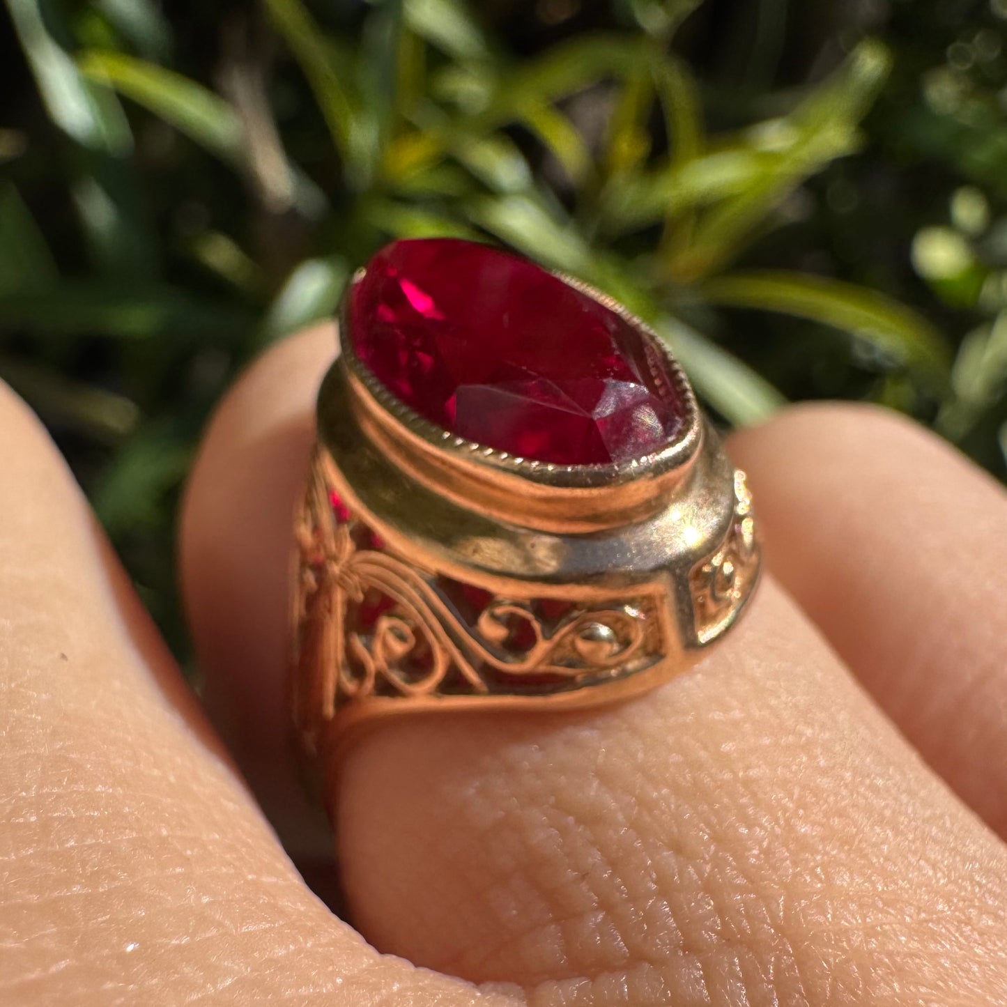 14K gold ring crowned with a vivid oval-cut Ruby, framed in an ornate bezel and accented by intricate filigree details