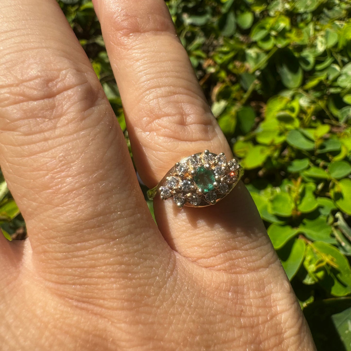 14K gold ring set with Emerald at its center, surrounded by a halo of brilliant-cut diamonds arranged in a floral-inspired cluster