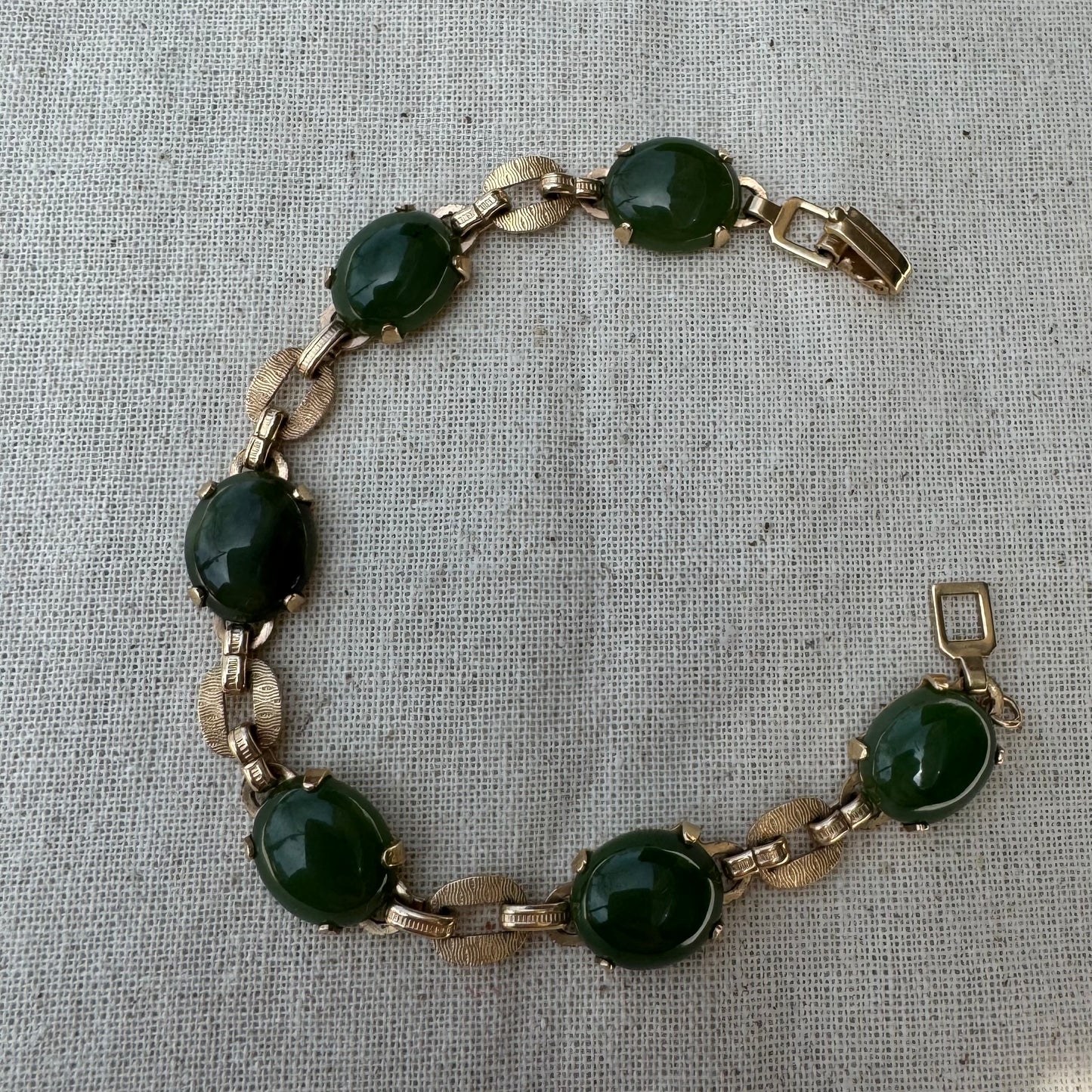 צמיד זהב צהוב 14 קראט משובץ באבני ג’ייד ירוקות בחיתוך קבושון (cabochon) בעיצוב אליפטי, המחוברות ביניהן בחוליות זהב עם טקסטורה מעניינת.