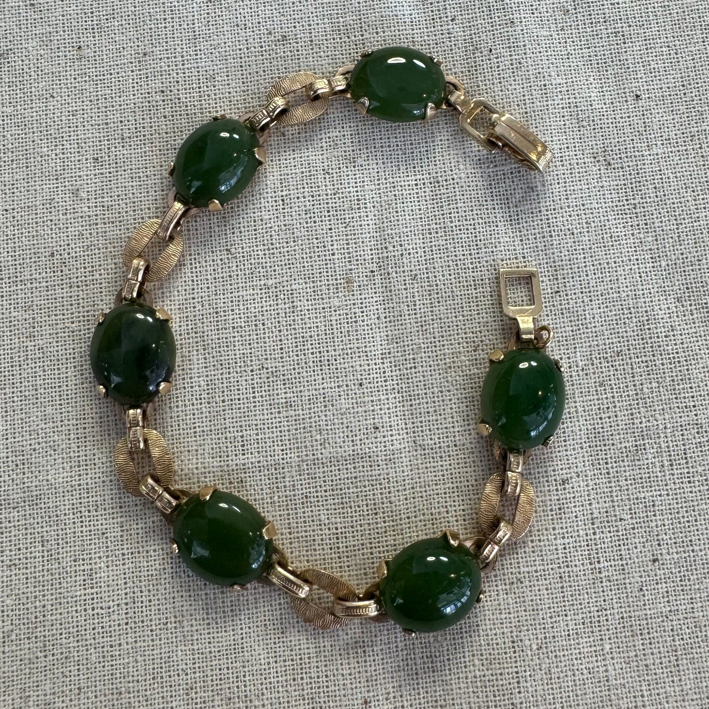 צמיד זהב צהוב 14 קראט משובץ באבני ג’ייד ירוקות בחיתוך קבושון (cabochon) בעיצוב אליפטי, המחוברות ביניהן בחוליות זהב עם טקסטורה מעניינת.