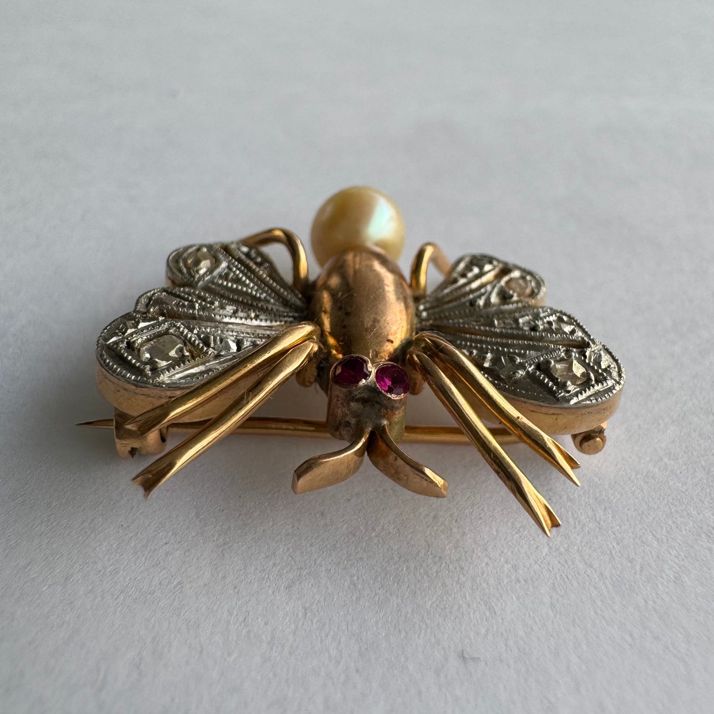 סיכת חרק ייחודית עשויה זהב 14 קראט משובצת יהלומים בעבודת פיליגרן עדינה בכנפיים, אבני רובי אדומות בעיניים ופנינה טבעית בגוון שמפניה.